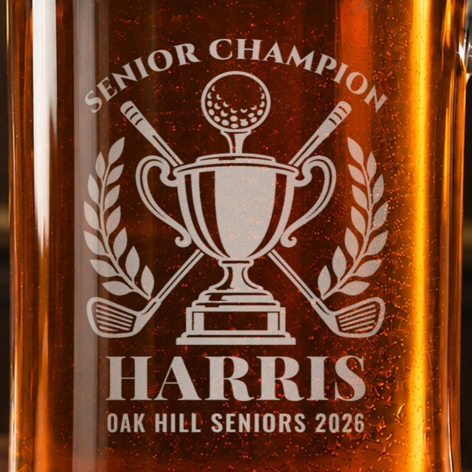 Close-up of the frosted golf trophy engraving on the stein: a trophy with a golf ball, crossed clubs and laurel, Senior Champion, Harris, Oak Hill Seniors 2026