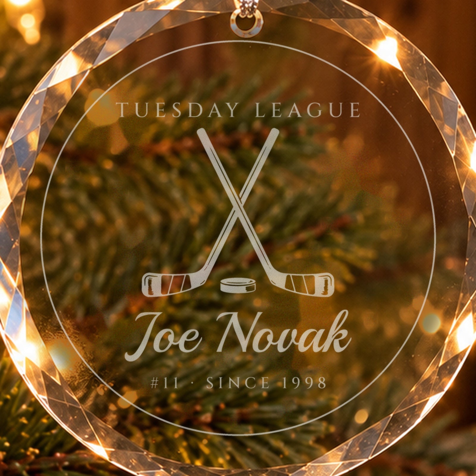 Close-up of the frosted engraving on the hockey Christmas ornament: crossed sticks and a puck, TUESDAY LEAGUE, Joe Novak, #11 · SINCE 1998