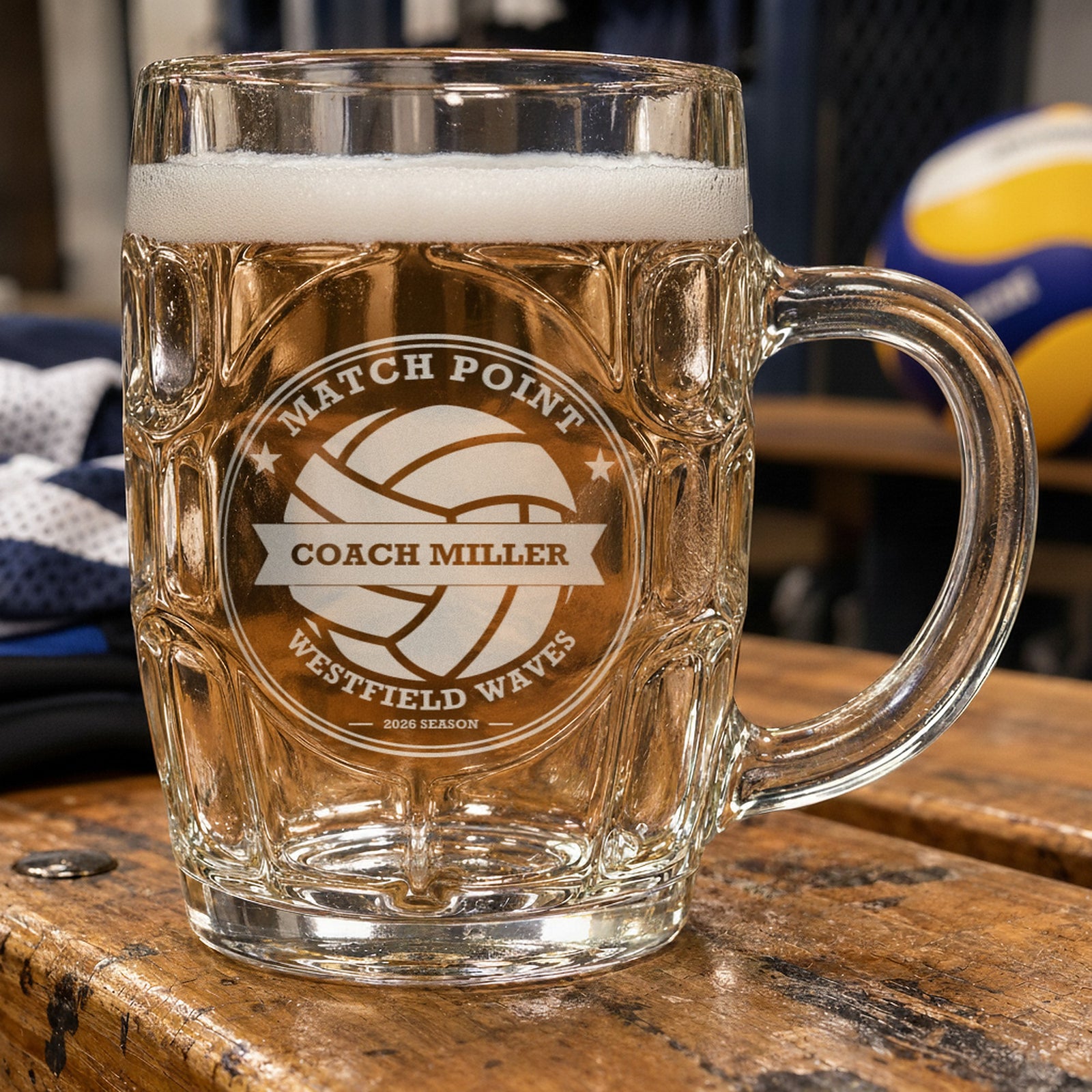 Personalized volleyball coach beer stein beside a volleyball and a pair of knee pads, frosted engraving reading Match Point, Coach Miller and Westfield Waves