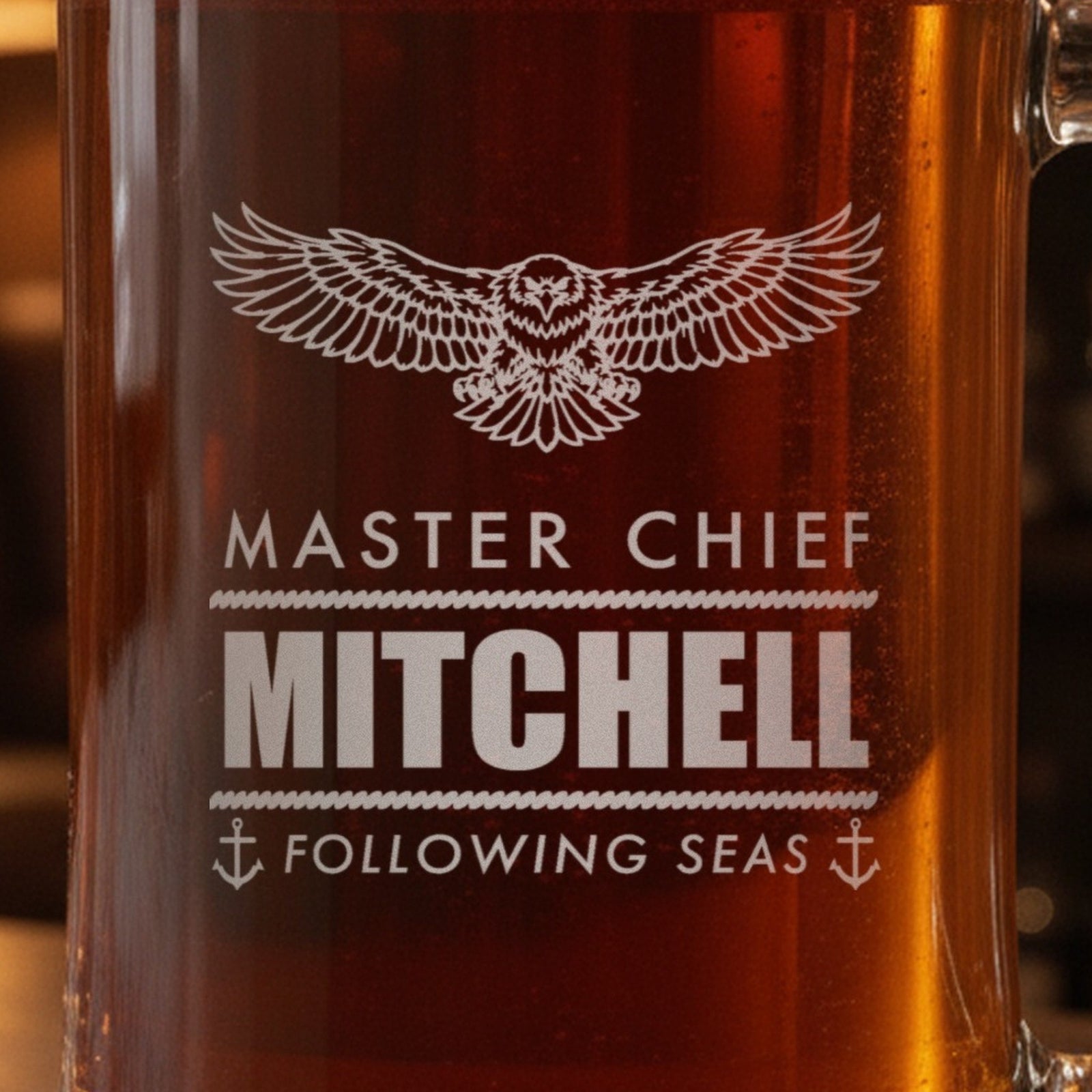 Close-up of the frosted eagle engraving on a retired Navy gift stein: Master Chief, Mitchell between two rope rules and Following Seas with anchors