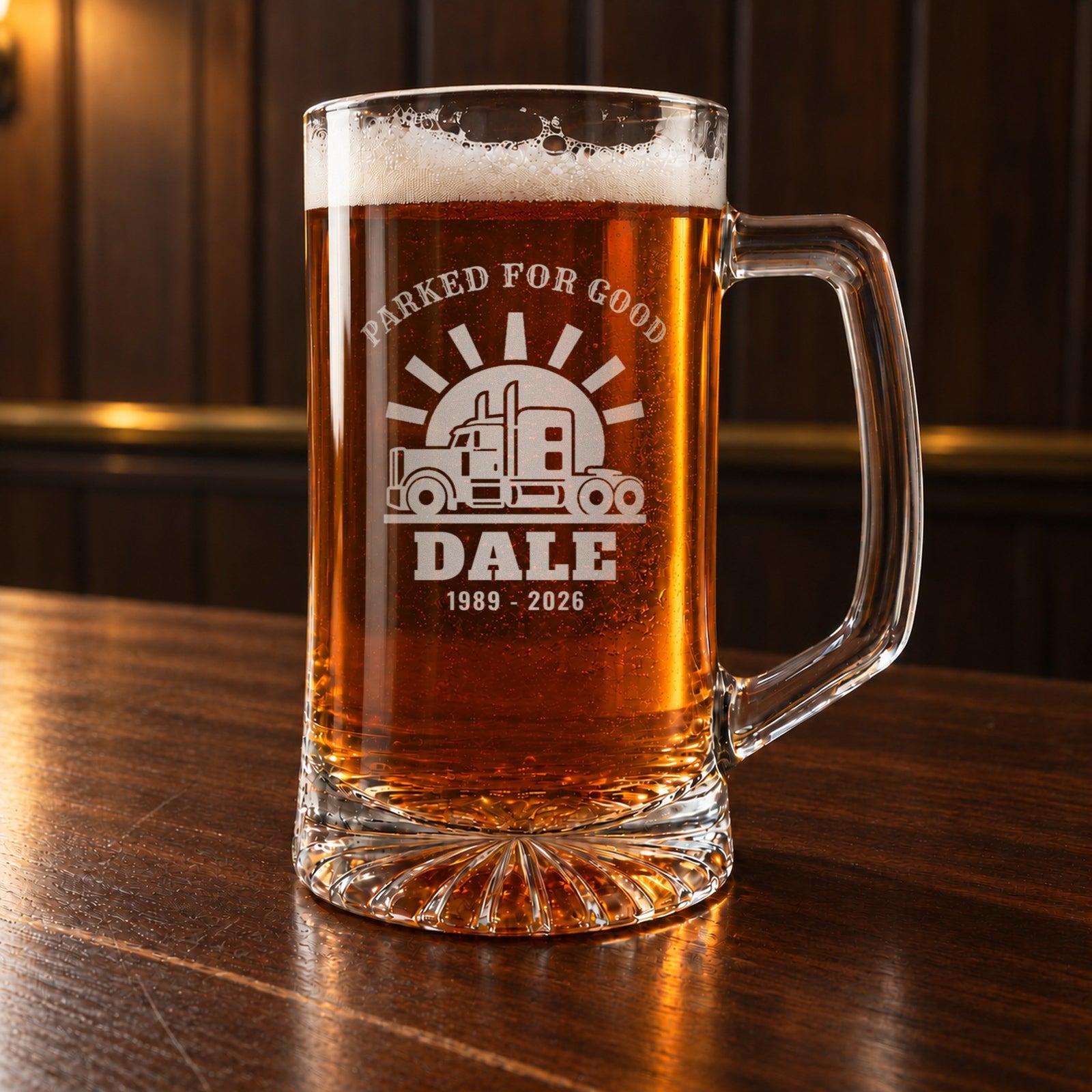 Trucker gift: a personalized 25 oz glass beer stein on a walnut bar, engraved PARKED FOR GOOD over a semi truck and setting sun, DALE and 1989 - 2026