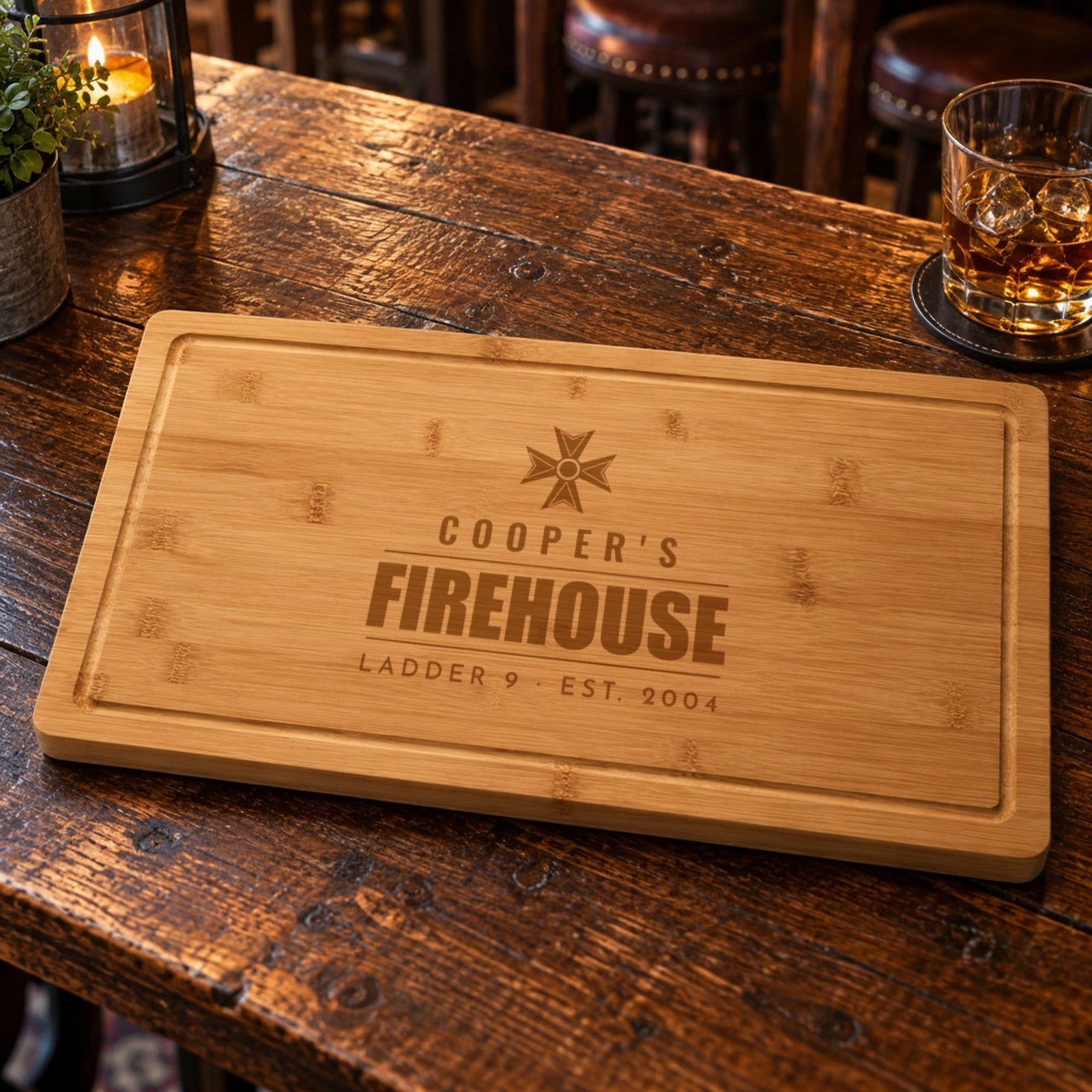 Personalized fireman gift, a bamboo cutting board engraved COOPER'S FIREHOUSE LADDER 9 EST. 2004 on a rustic tavern table with a whiskey