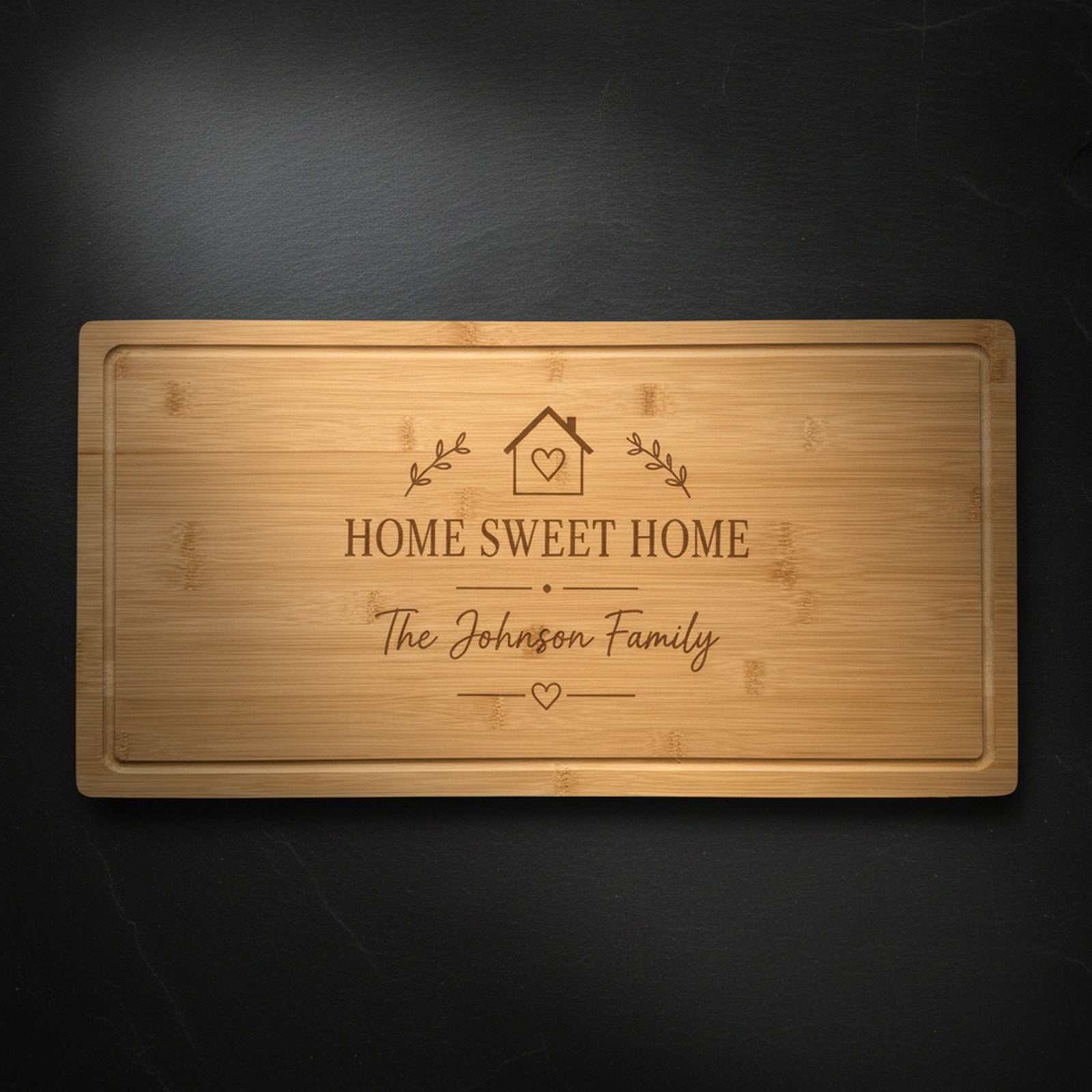Personalized housewarming cutting board in solid bamboo on dark slate, laser engraved with a Home Sweet Home crest above the family name.
