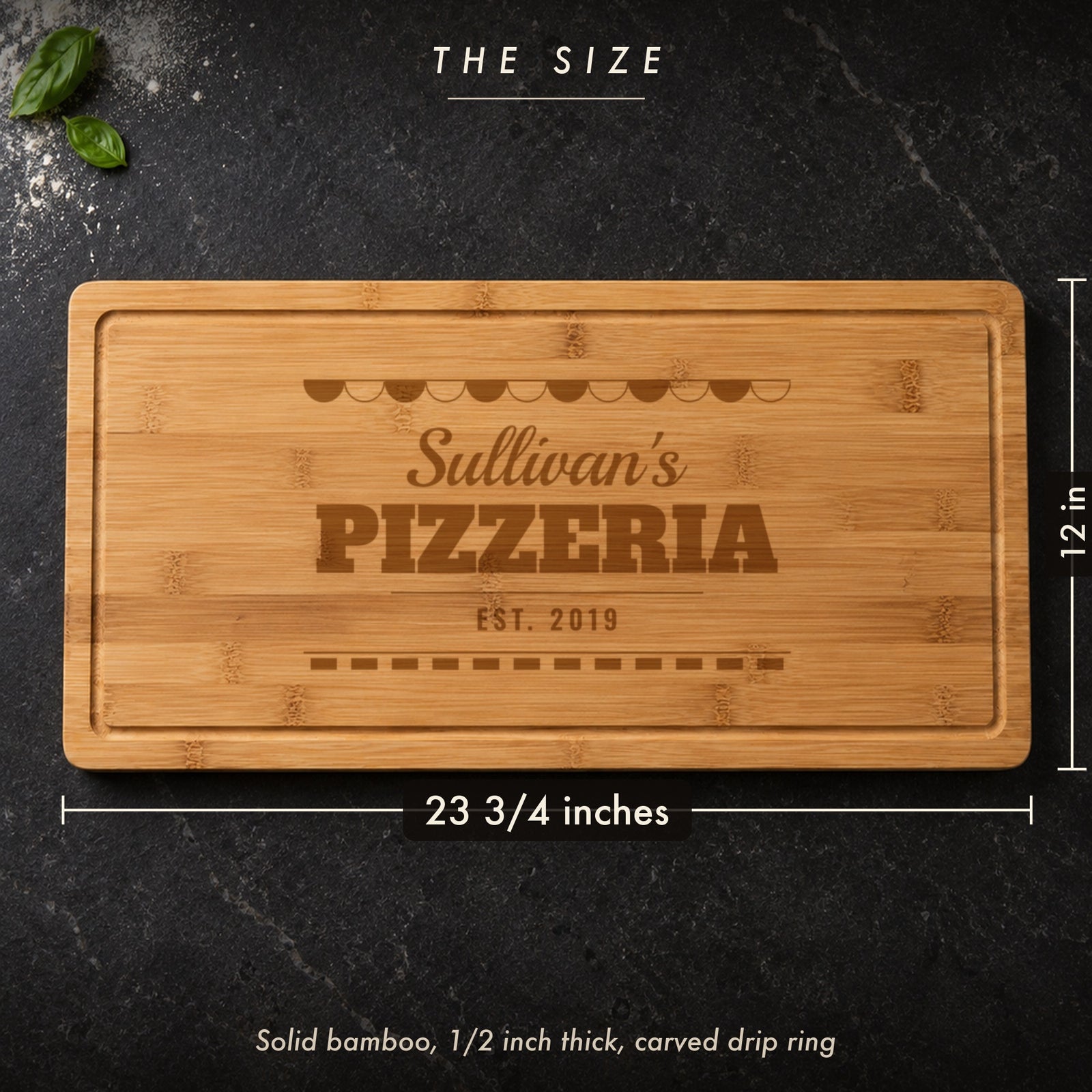 Size of the personalized pizza cutting board, 23 3/4 inches long by 12 inches wide in half inch solid bamboo, shown on a dark kitchen counter