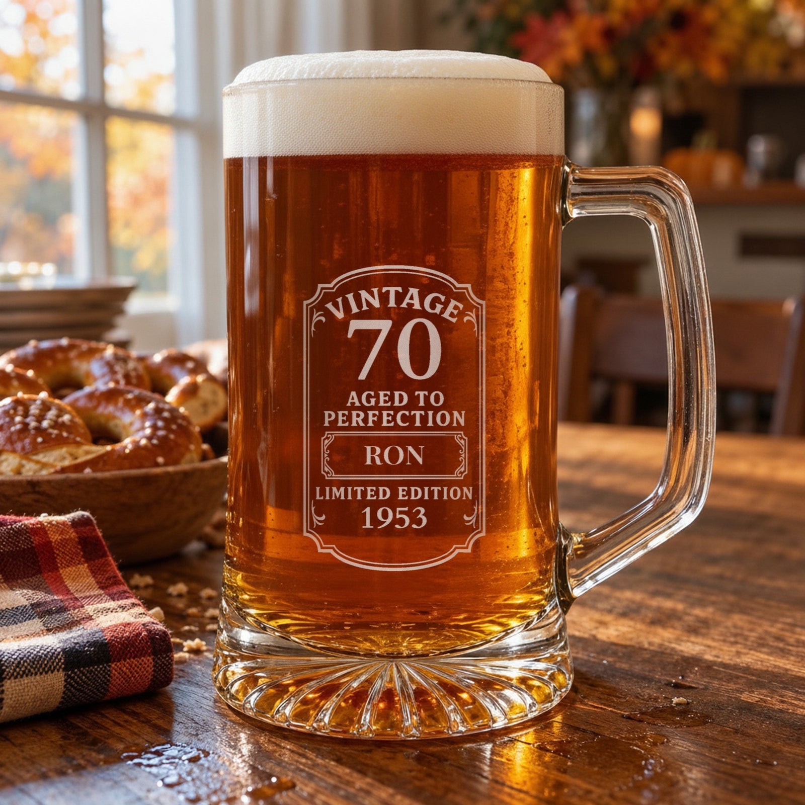 Engraved 70th birthday beer stein of amber lager on an autumn kitchen table, the Vintage 70 label personalized for Ron, born 1953