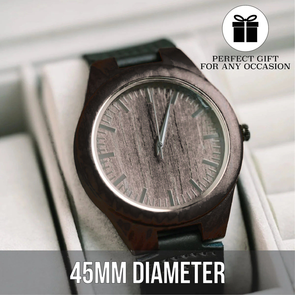 Dark ebony sandalwood watch resting in a white cushioned display case, angled so the wood grain dial, silver bezel ring and black leather strap are visible