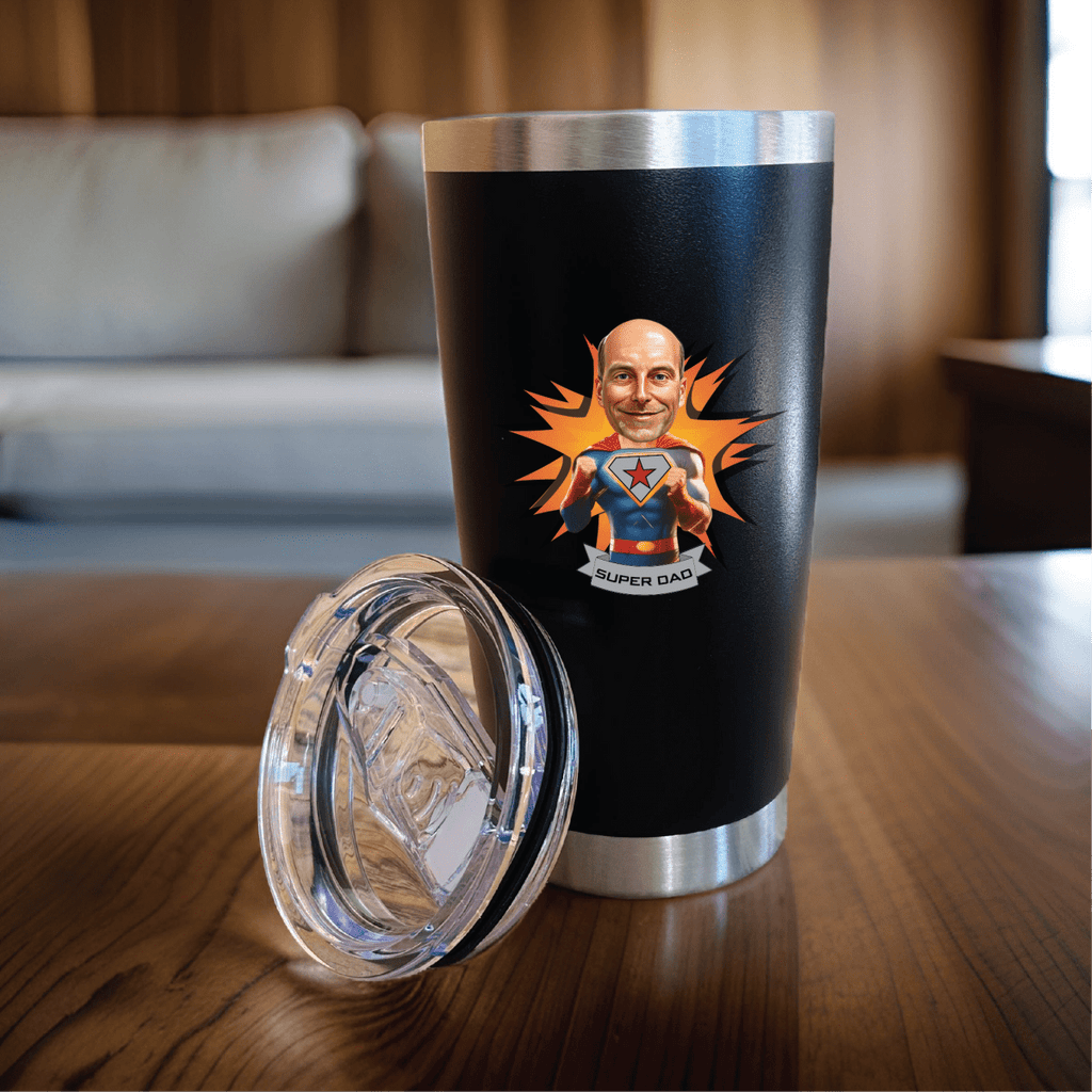 Personalized black stainless tumbler printed with a custom superhero caricature and Super Dad text, shown with its clear lid on a wooden table.