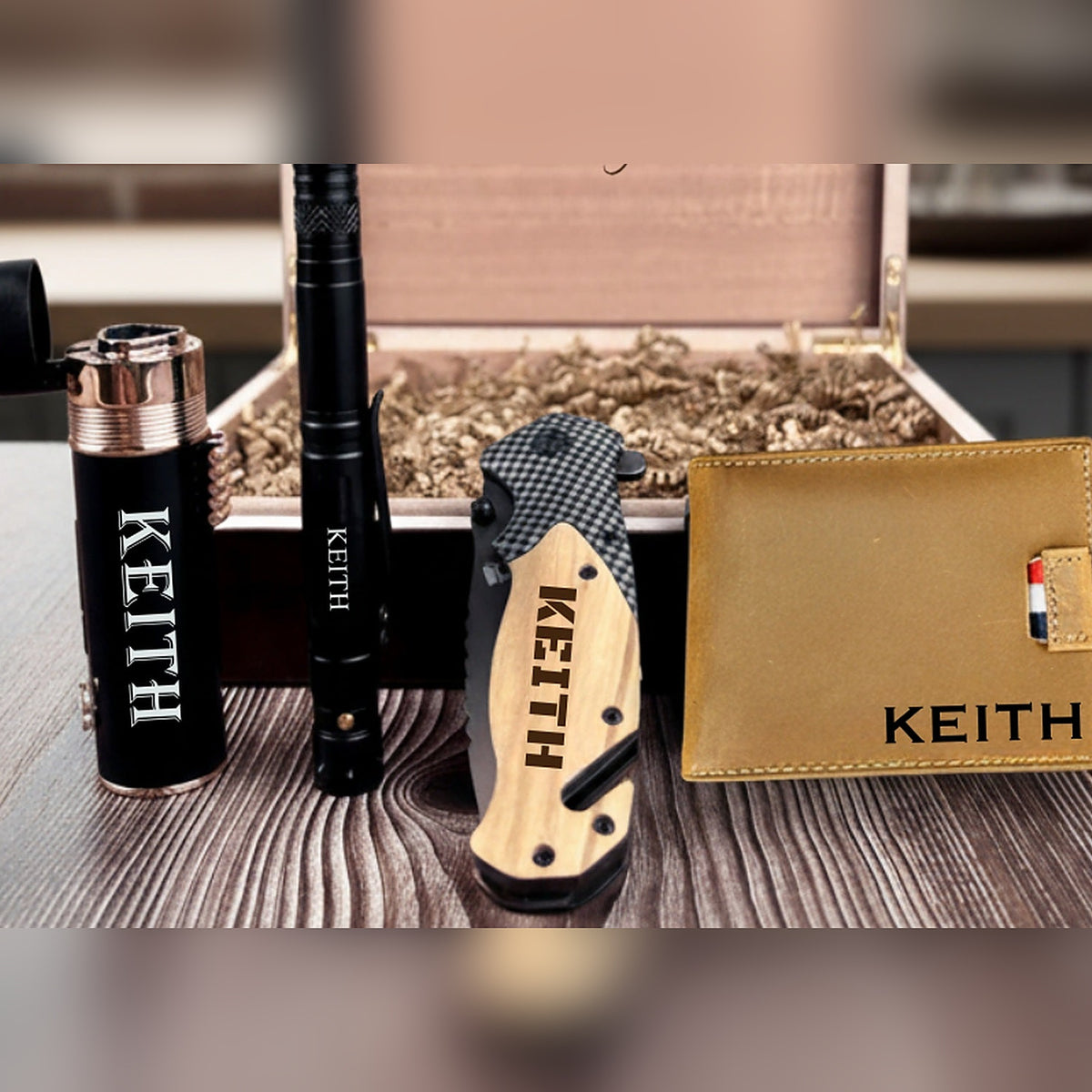 Open military keepsake gift box showing the engraved folding knife, leather wallet, torch lighter and tactical pen on paper shred.
