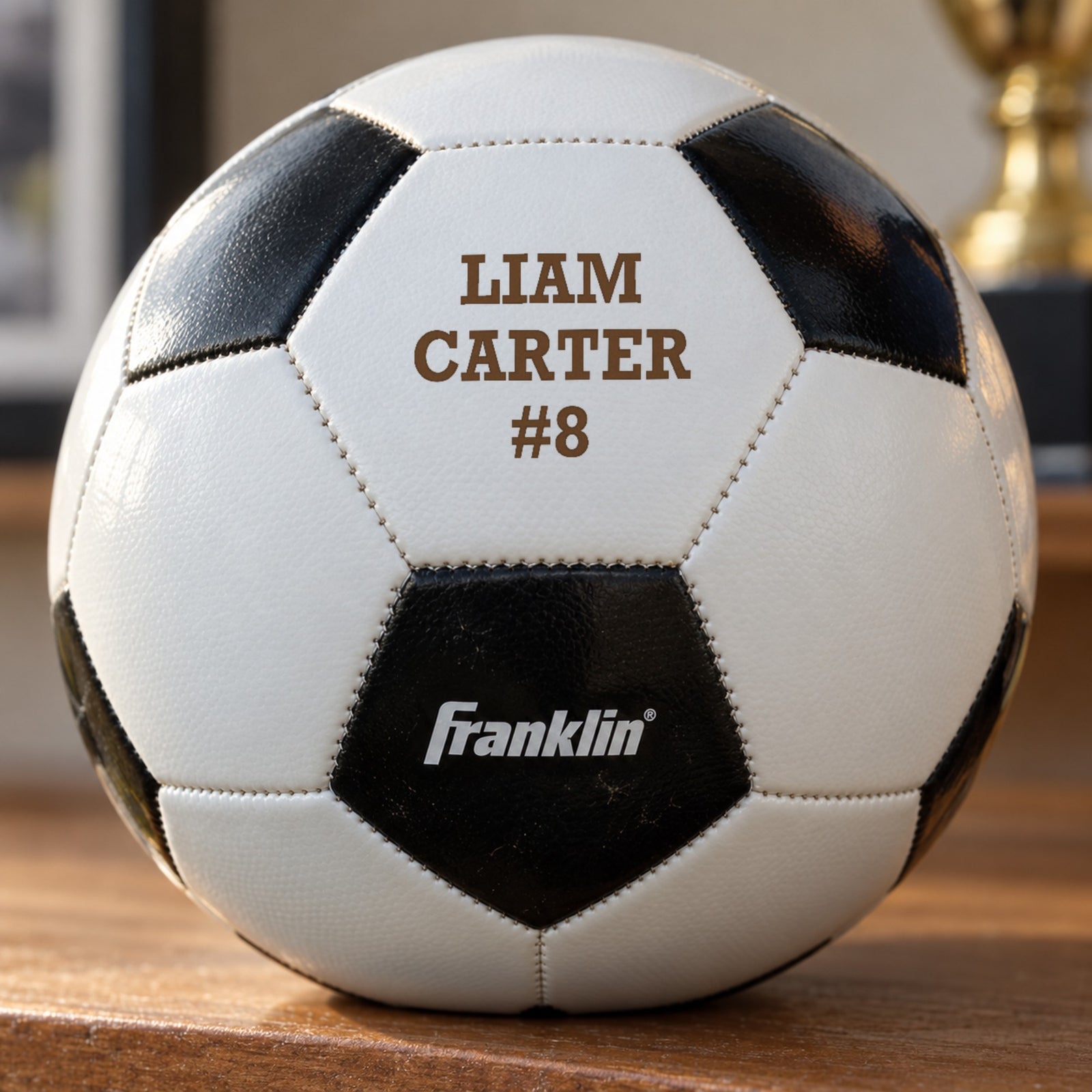 Close-up of a soccer ball panel laser engraved in warm brown with the name Liam Carter and number 8, a personalized senior soccer gift