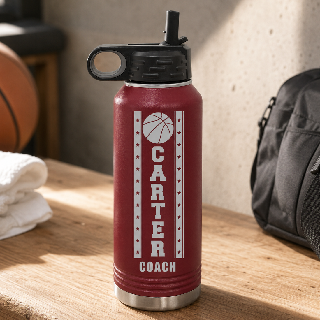 Red insulated water bottle with black flip-top lid, engraved with sample text "CARTER COACH" and basketball design with stars