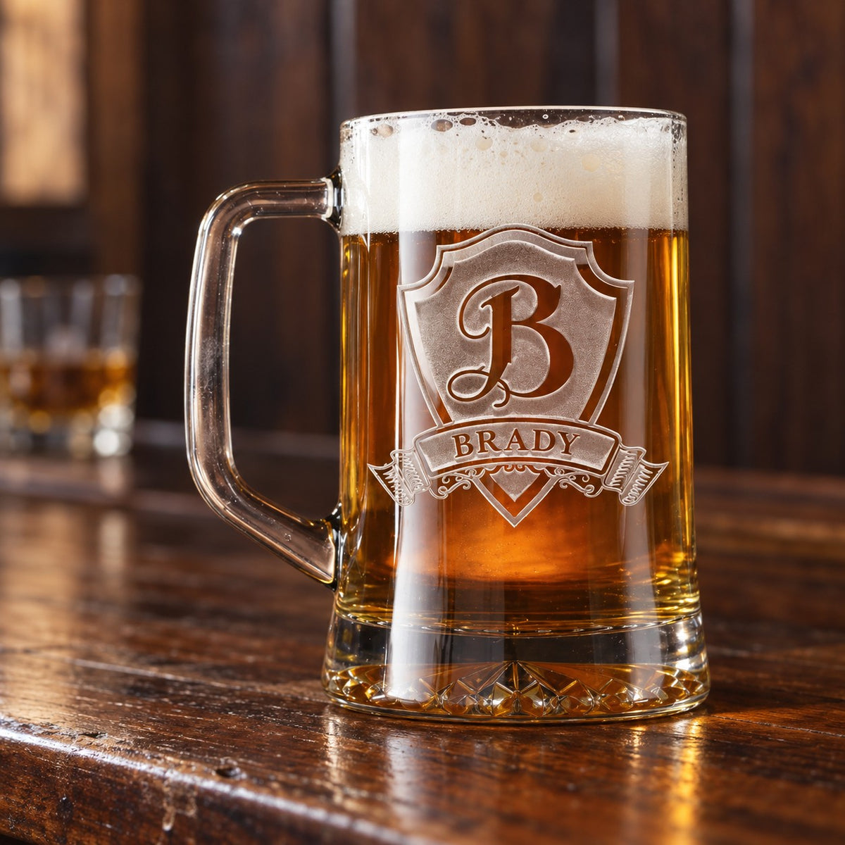 Personalized beer mug with a sand-carved shield, a large initial B and the name BRADY on the banner, filled with lager on a walnut home bar.