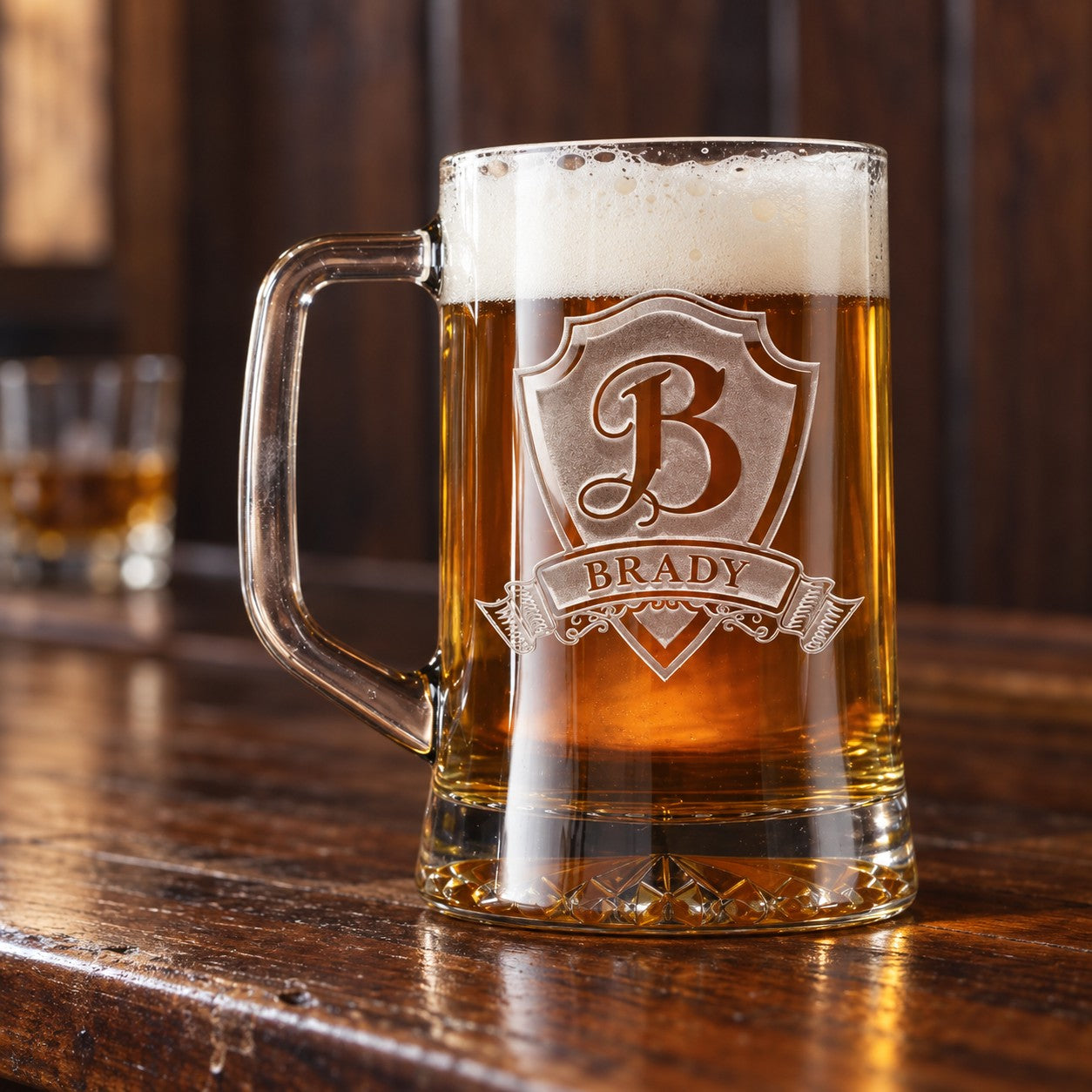 Personalized beer mug with a sand-carved shield, a large initial B and the name BRADY on the banner, filled with lager on a walnut home bar.