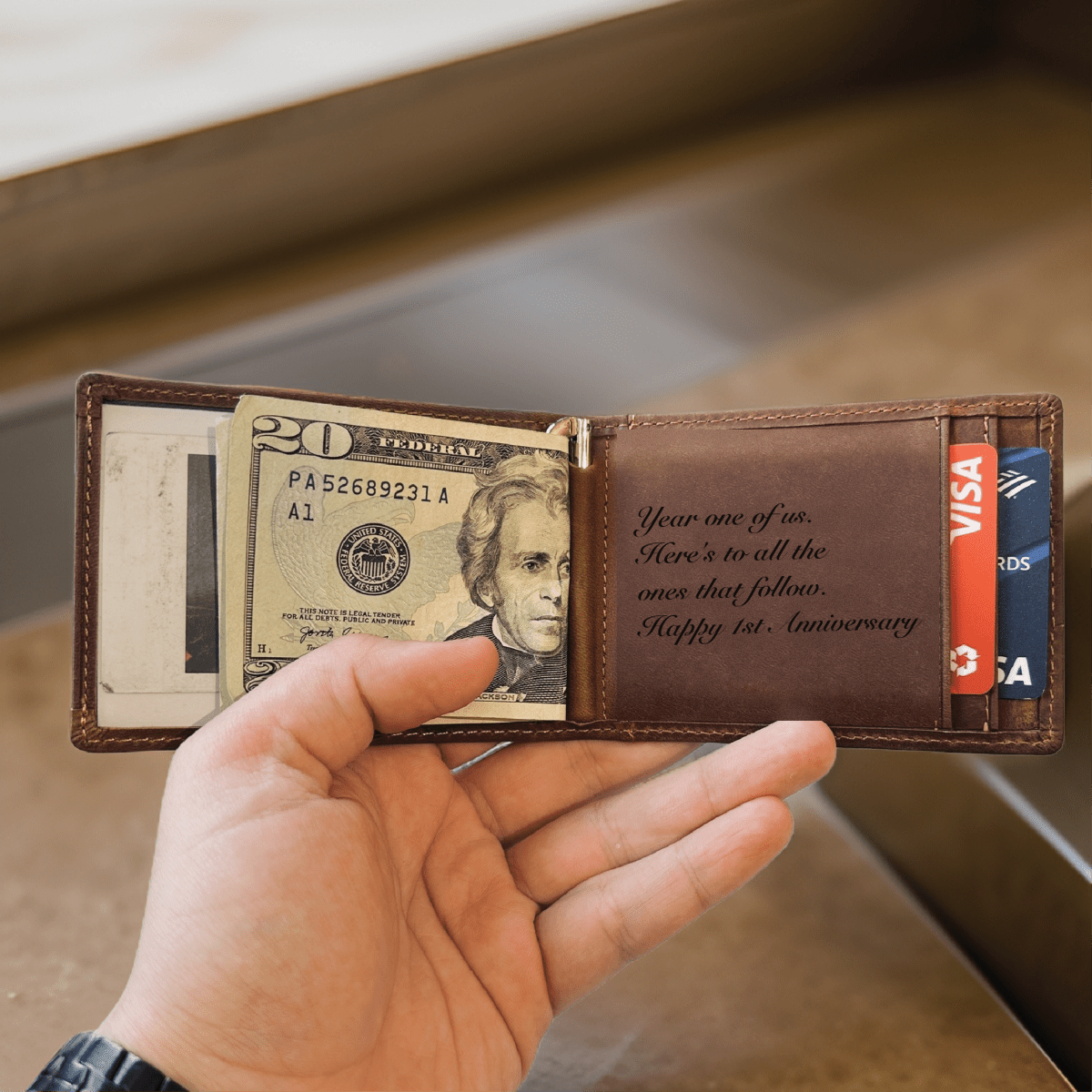 Personalized leather wallet held open showing a first anniversary message laser-engraved inside the brown leather panel in script lettering.