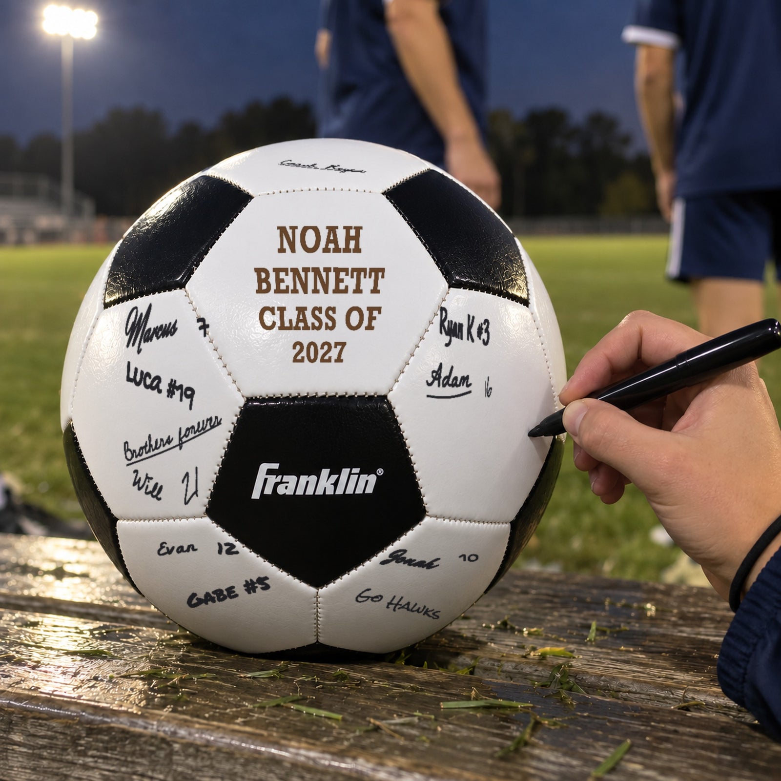 Teammate signing a personalized soccer ball engraved for Noah Bennett, Class of 2027, on the bench after the game, one of the best soccer senior night gift ideas
