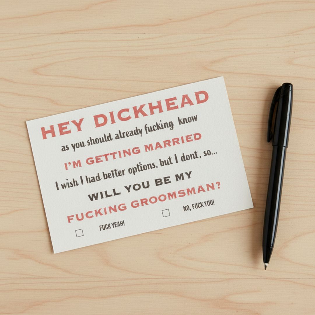 Humorous groomsmen proposal card with crude text asking "Will you be my fucking groomsman?" and checkbox options for "Fuck yeah!" or "No, fuck you!", displayed on light wood surface with black pen.