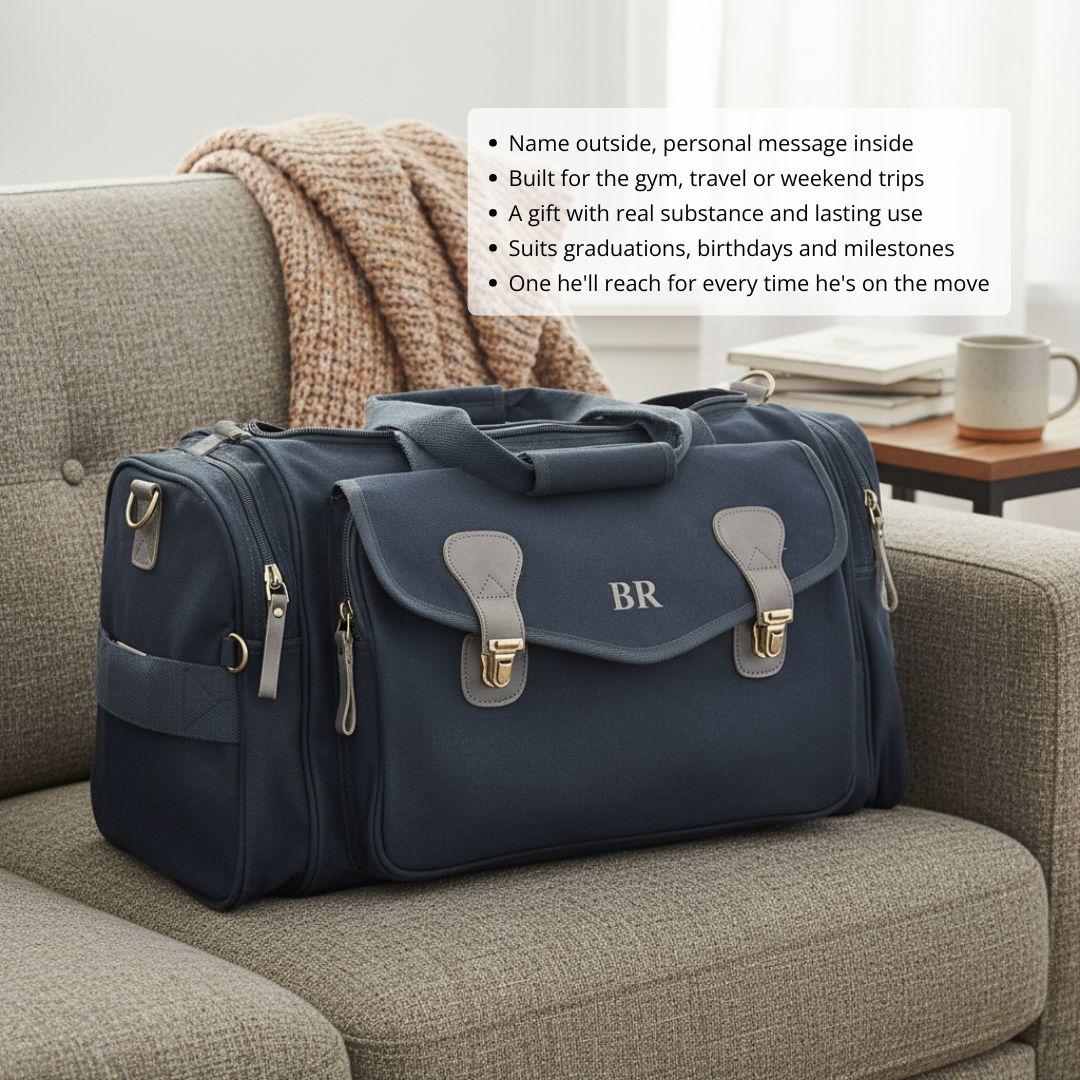 Navy duffle bag with gray leather handles and brass closures, featuring sample monogram "BR" embroidered on front flap, displayed on gray sofa