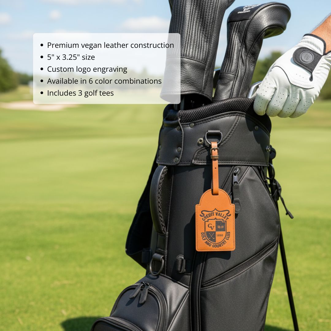 Golf bag tag in orange vegan leather with sample engraved logo design, attached to black golf bag on course with clubs and gloved hands visible