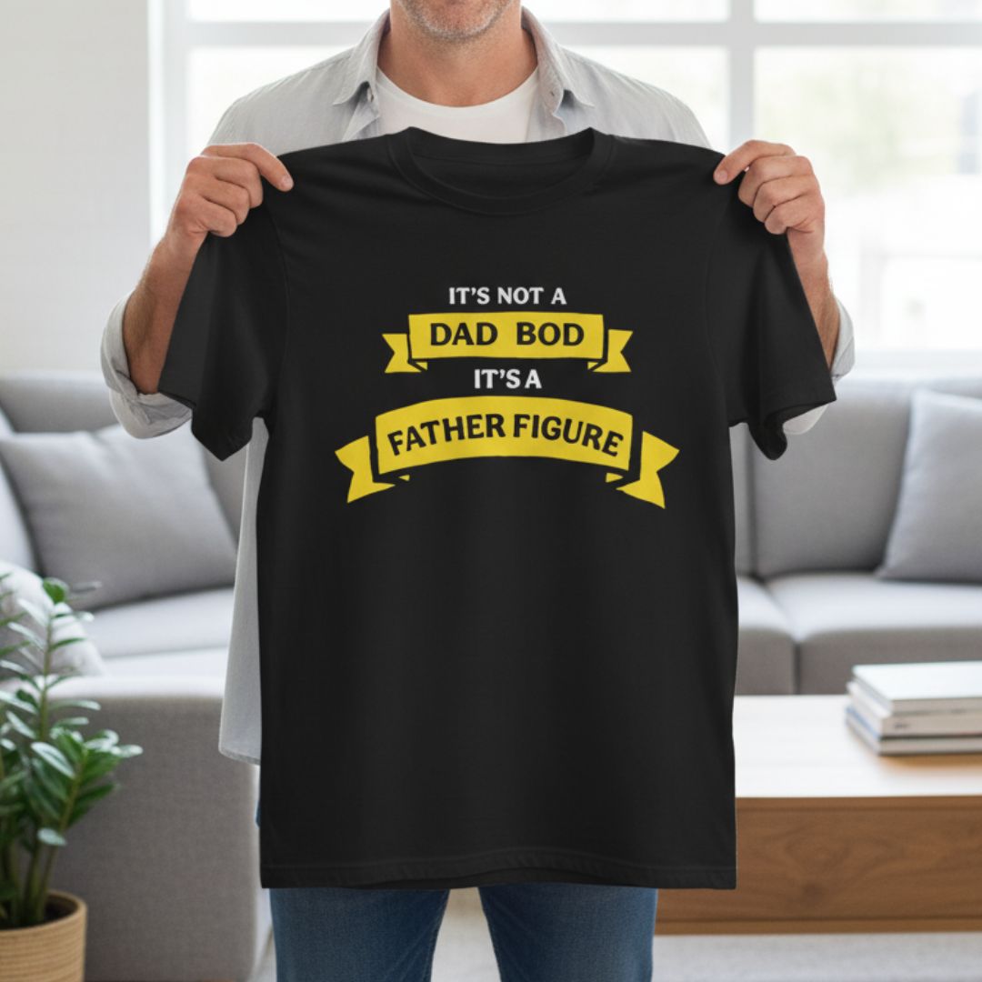 Black t-shirt with yellow banner design reading "It's not a dad bod, it's a father figure" displayed on model indoors