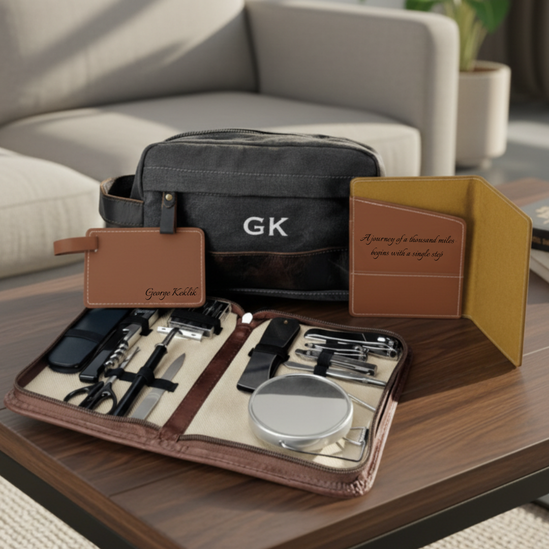 Travel gift set shown with a dark canvas wash bag embroidered GK, a leather passport holder engraved with a quotation, a luggage tag and an open grooming case on a coffee table