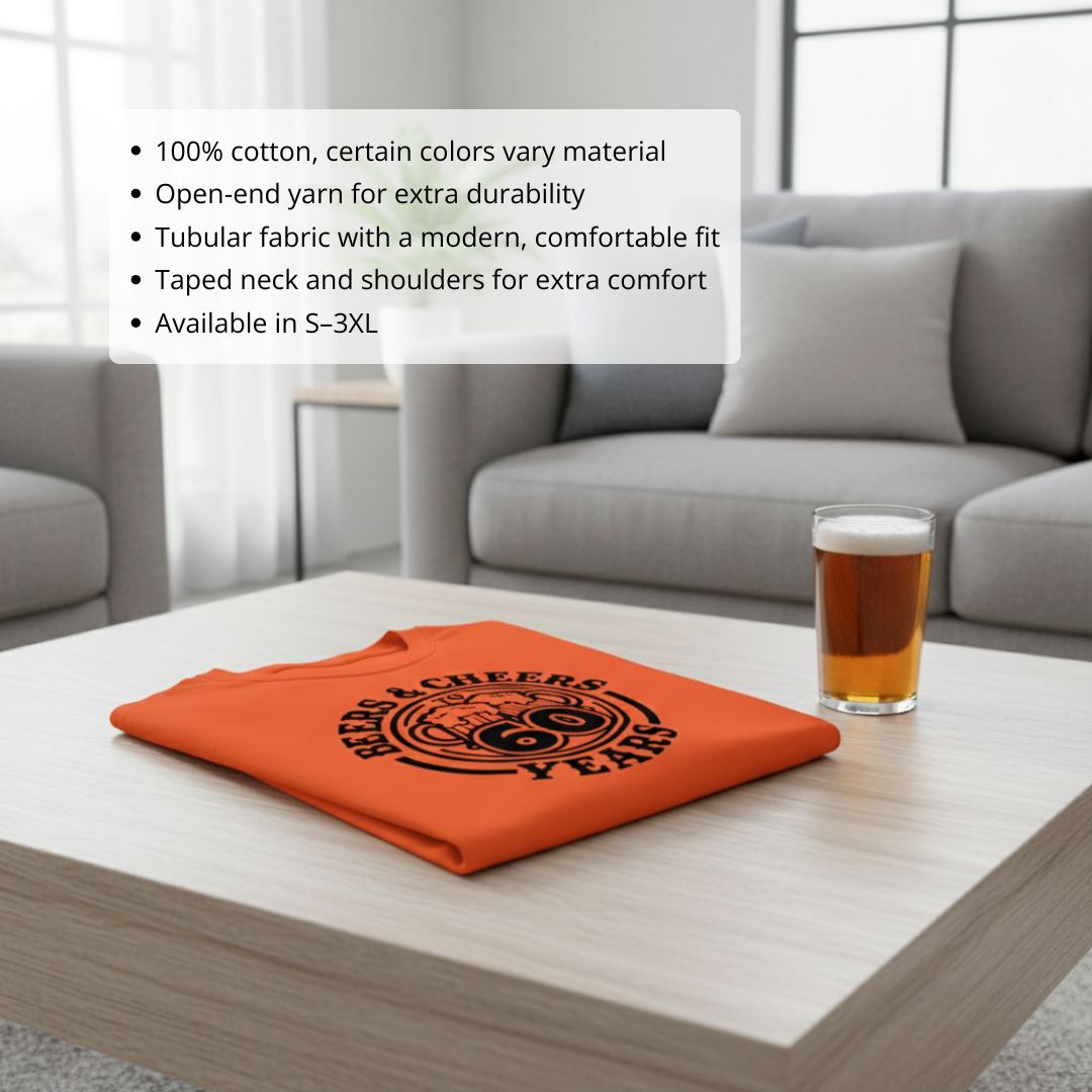 Bright orange t-shirt folded on table with black "Beers & Cheers to 60 Years" circular design, displayed next to beer glass in living room setting