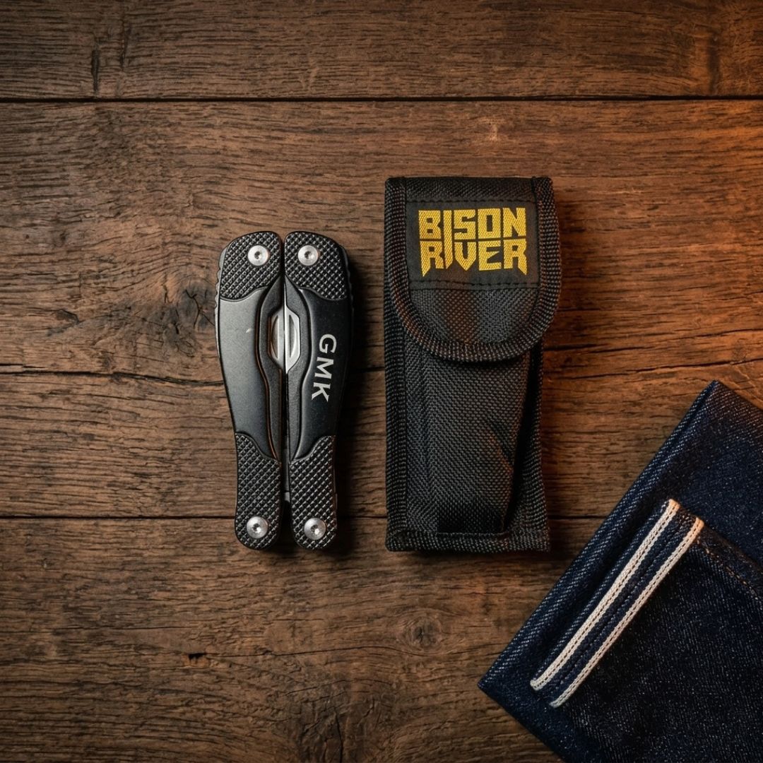 Compact folded multi-tool with carbon fiber handle displaying GMK branding, shown alongside black nylon carry pouch labeled "Bison River" and navy tactical pouch on wooden surface