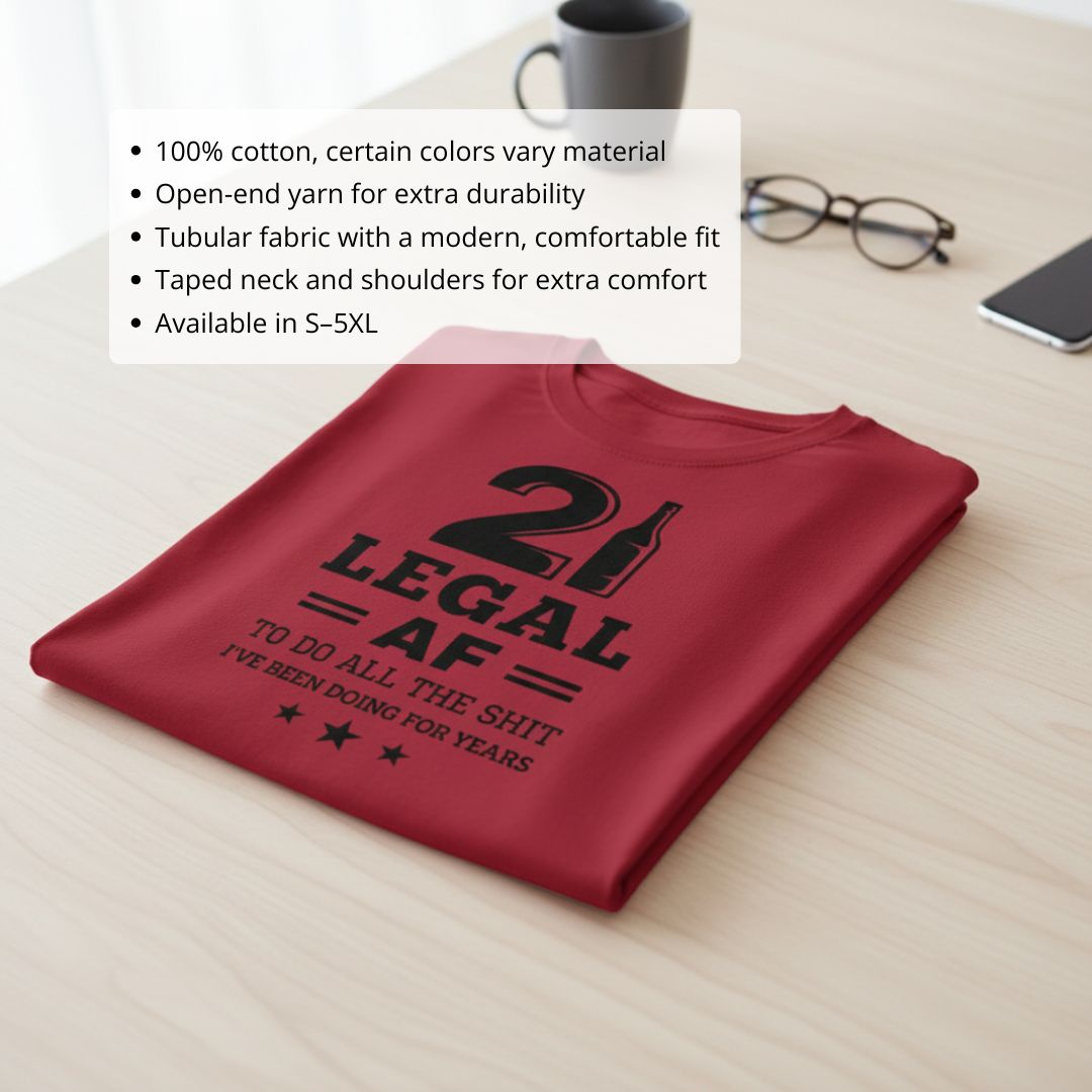 Burgundy t-shirt printed with "21 LEGAL AF" text and "TO DO ALL THE SHIT I'VE BEEN DOING FOR YEARS" with star accents, folded flat lay on wooden surface
