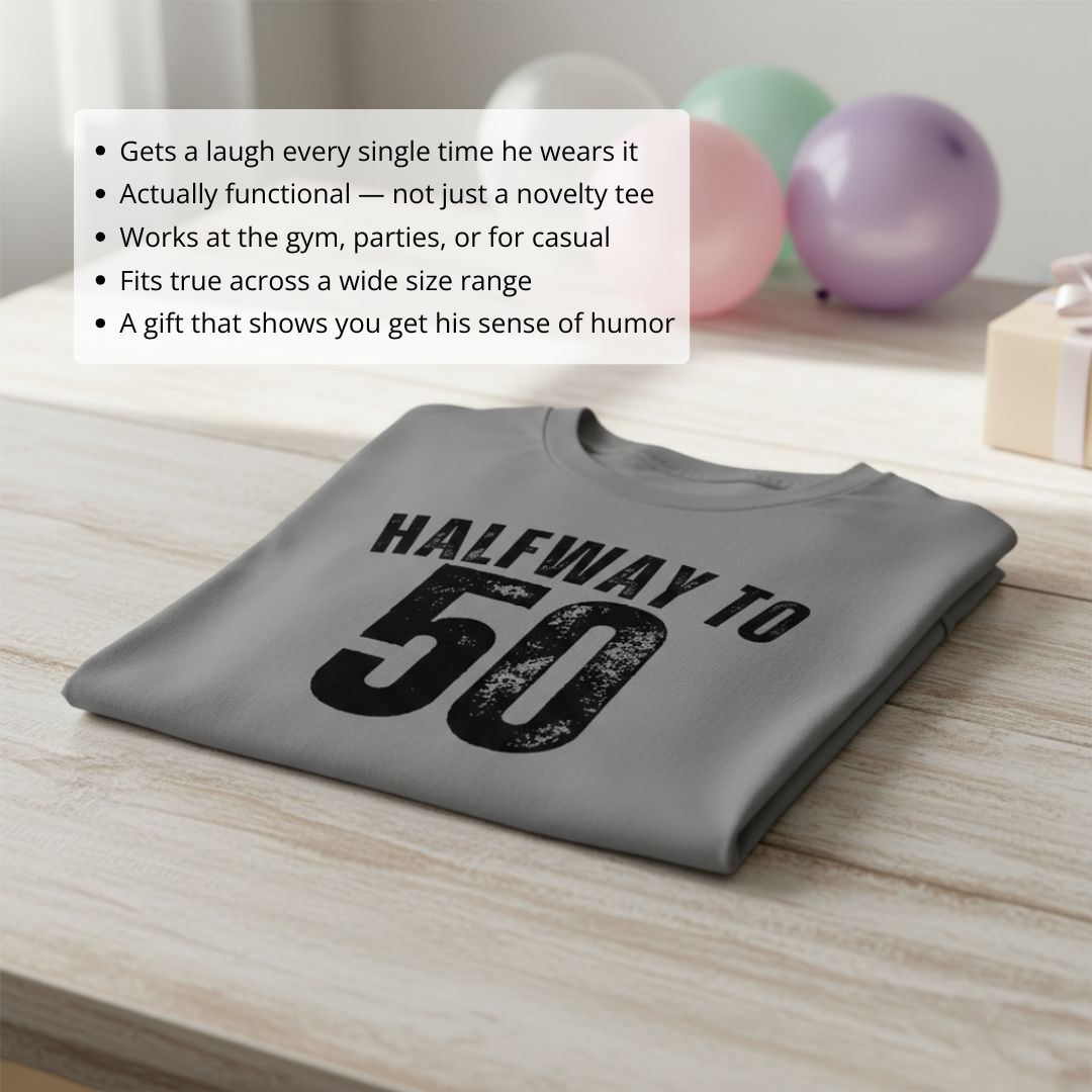 Gray t-shirt with black distressed print reading "Halfway to 50" laid flat on wooden surface with colorful balloons in background
