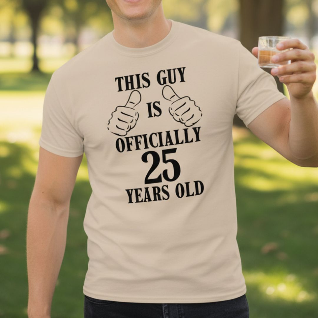 Cream t-shirt with "This Guy is Officially 25 Years Old" text and thumbs-up graphic, worn outdoors while holding a whiskey glass