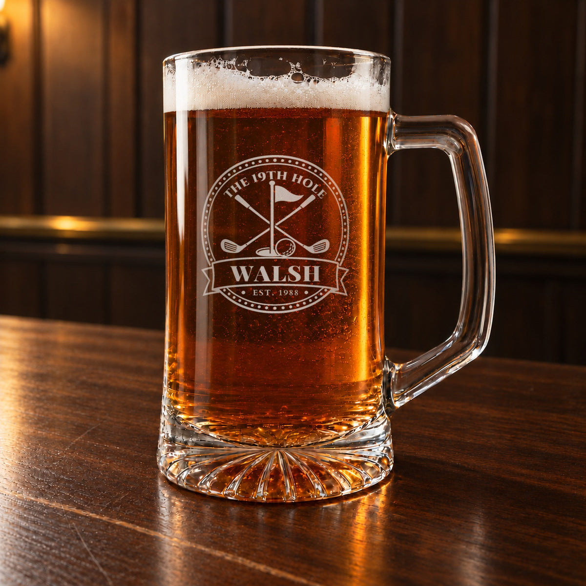 Personalized 19th hole golf beer stein on a walnut bar, engraved with a golf flag, crossed clubs and a golf ball in a round badge: The 19th Hole, Walsh, Est. 1988