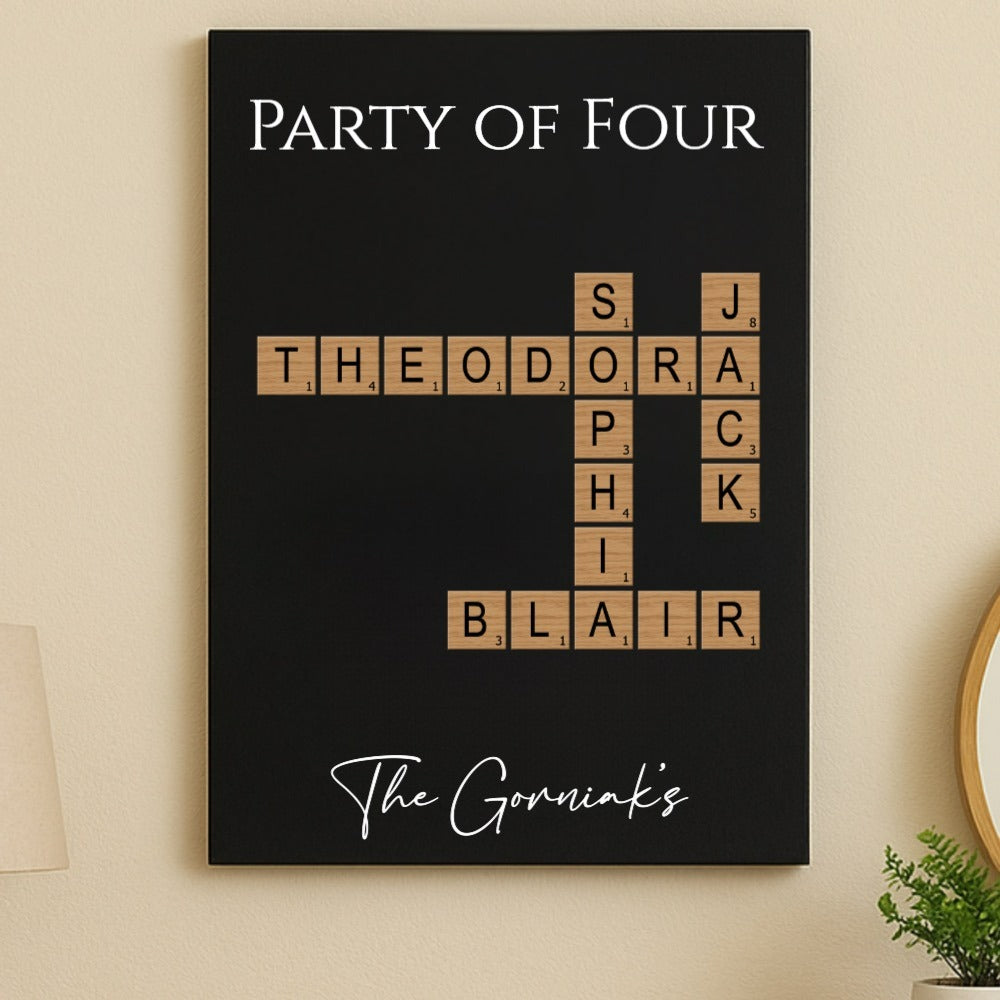 Black wall sign with "Party of Four" text at top, wood-grain Scrabble-style tiles arranged in crossword pattern spelling sample names "Theodora," "Blair," and initials, with "The Gorniaks" printed at bottom in script.