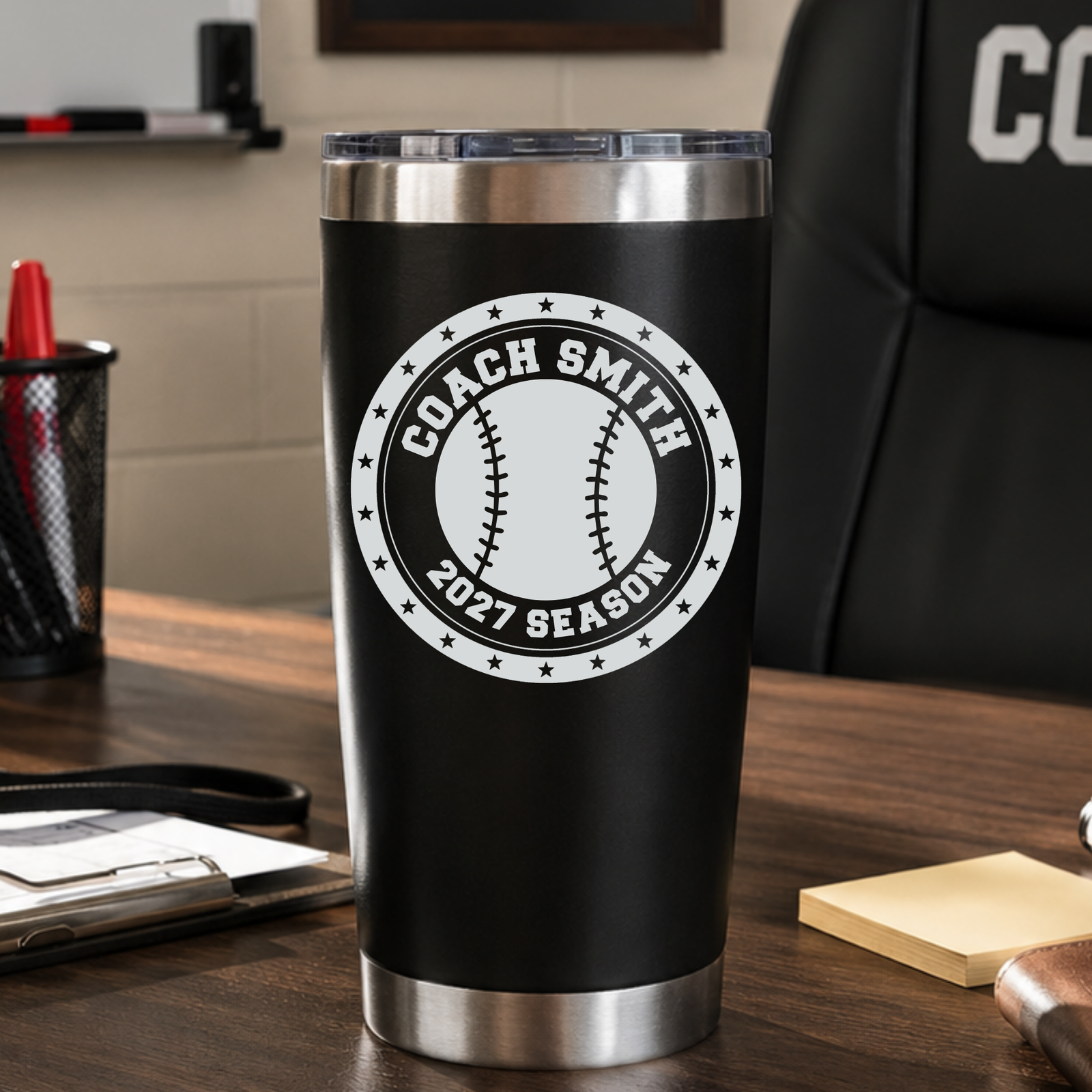 Black baseball coach tumbler engraved with COACH SMITH and 2027 SEASON, sitting on a coach's desk, a personalized end-of-season baseball gift