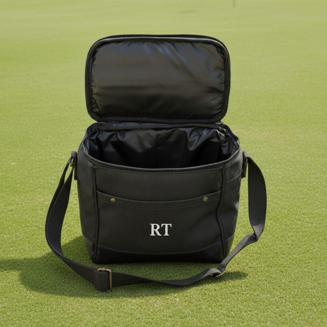 Black insulated cooler bag opened to show interior, monogrammed with sample initials "RT" on front, featuring adjustable shoulder strap and brass hardware accents