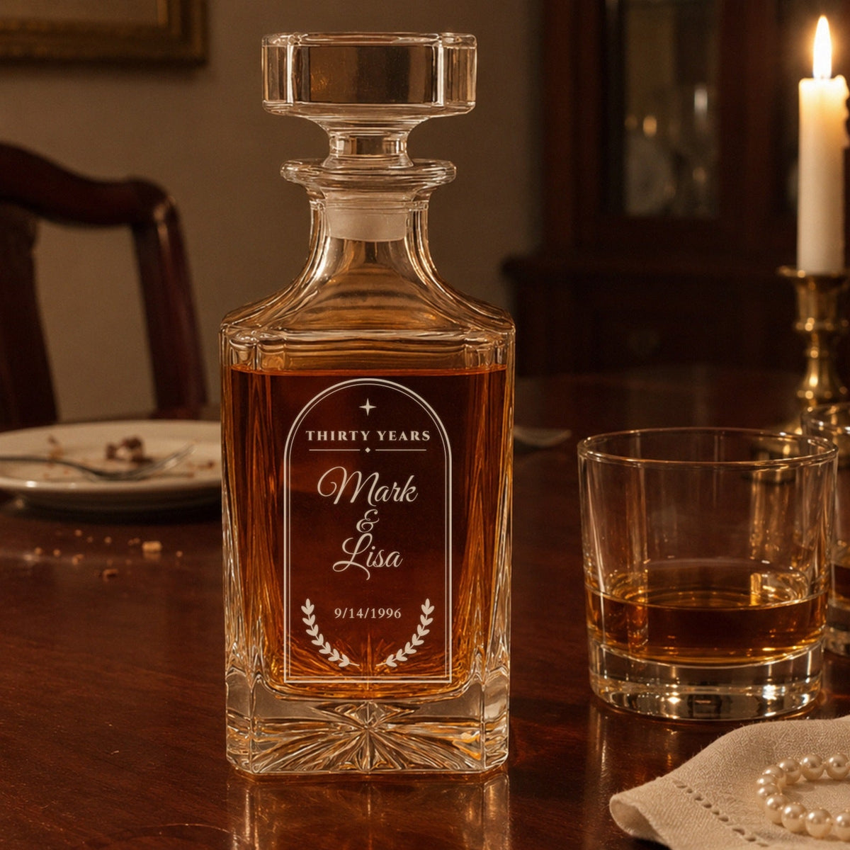 Engraved 30 year anniversary decanter for Mark and Lisa on a candlelit dining table with two bourbons and a strand of pearls on a linen napkin