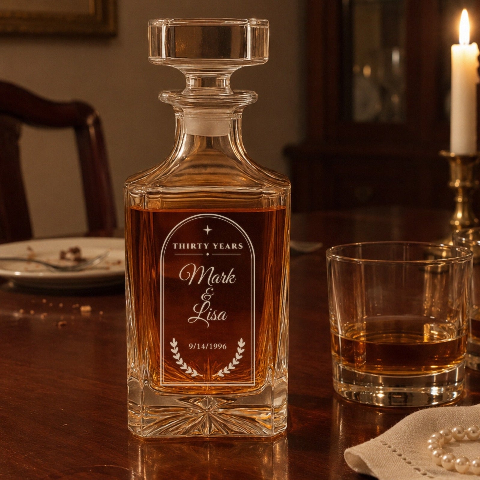 Engraved 30 year anniversary decanter for Mark and Lisa on a candlelit dining table with two bourbons and a strand of pearls on a linen napkin