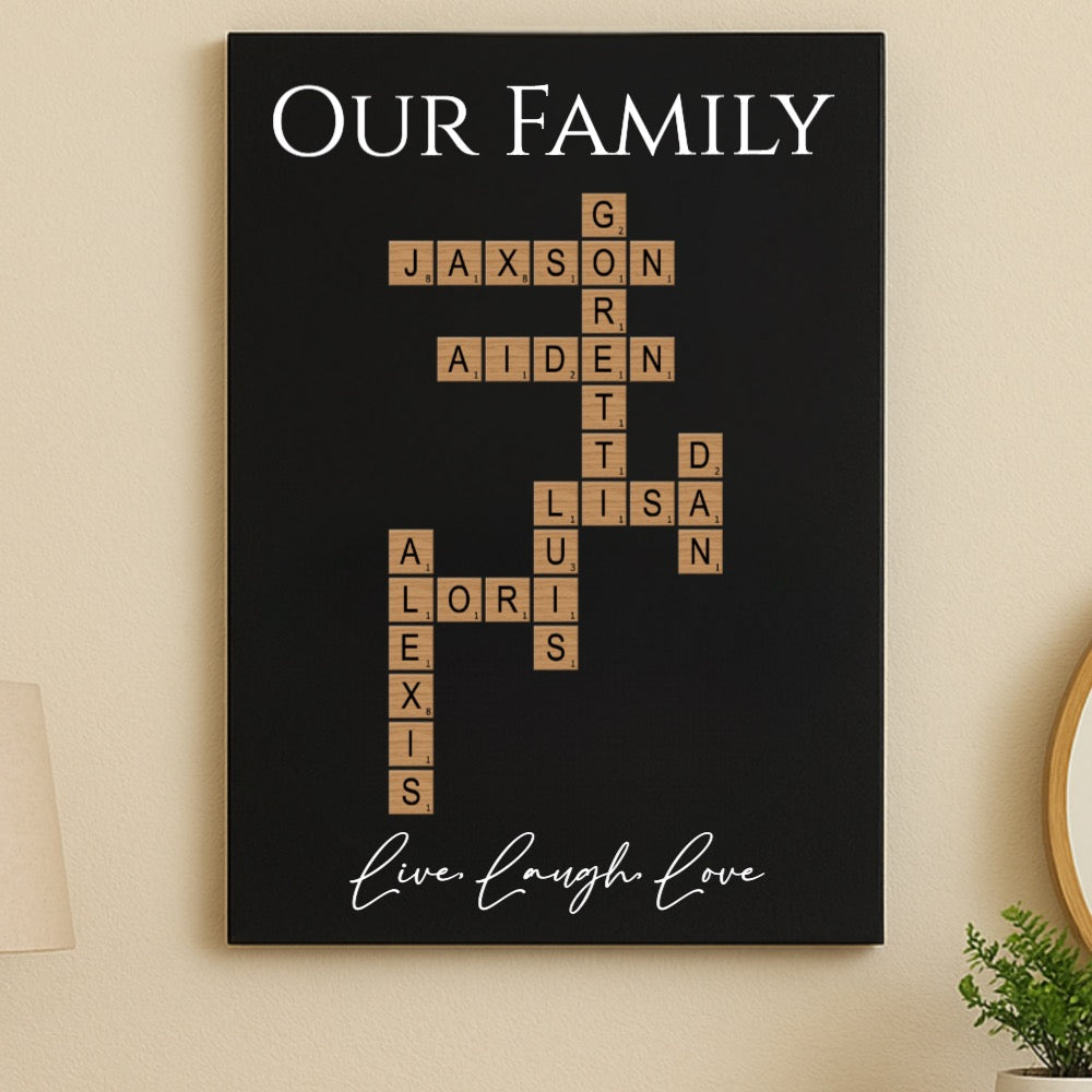 Black wall sign with "Our Family" heading and family names arranged in crossword pattern with sample names Jaxson, Aiden, Gar, Lisa, Lori, and Alexis, with "live laugh love" script at bottom