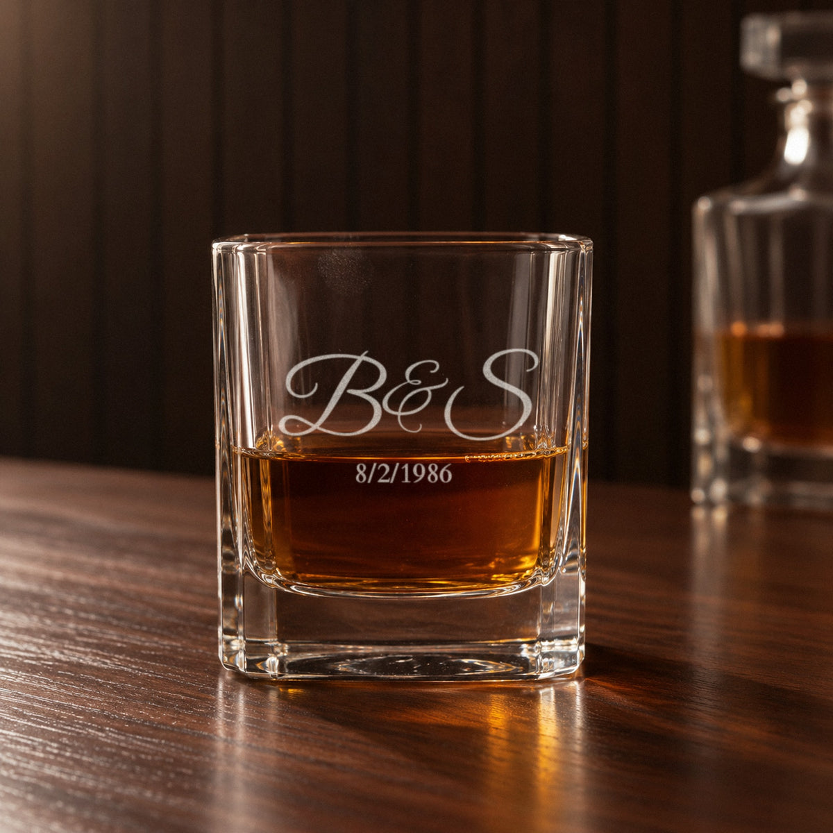 Close-up of an engraved rocks glass from the personalized whiskey decanter set, frosted initials B&S and the date 8/2/1986 with whiskey showing through