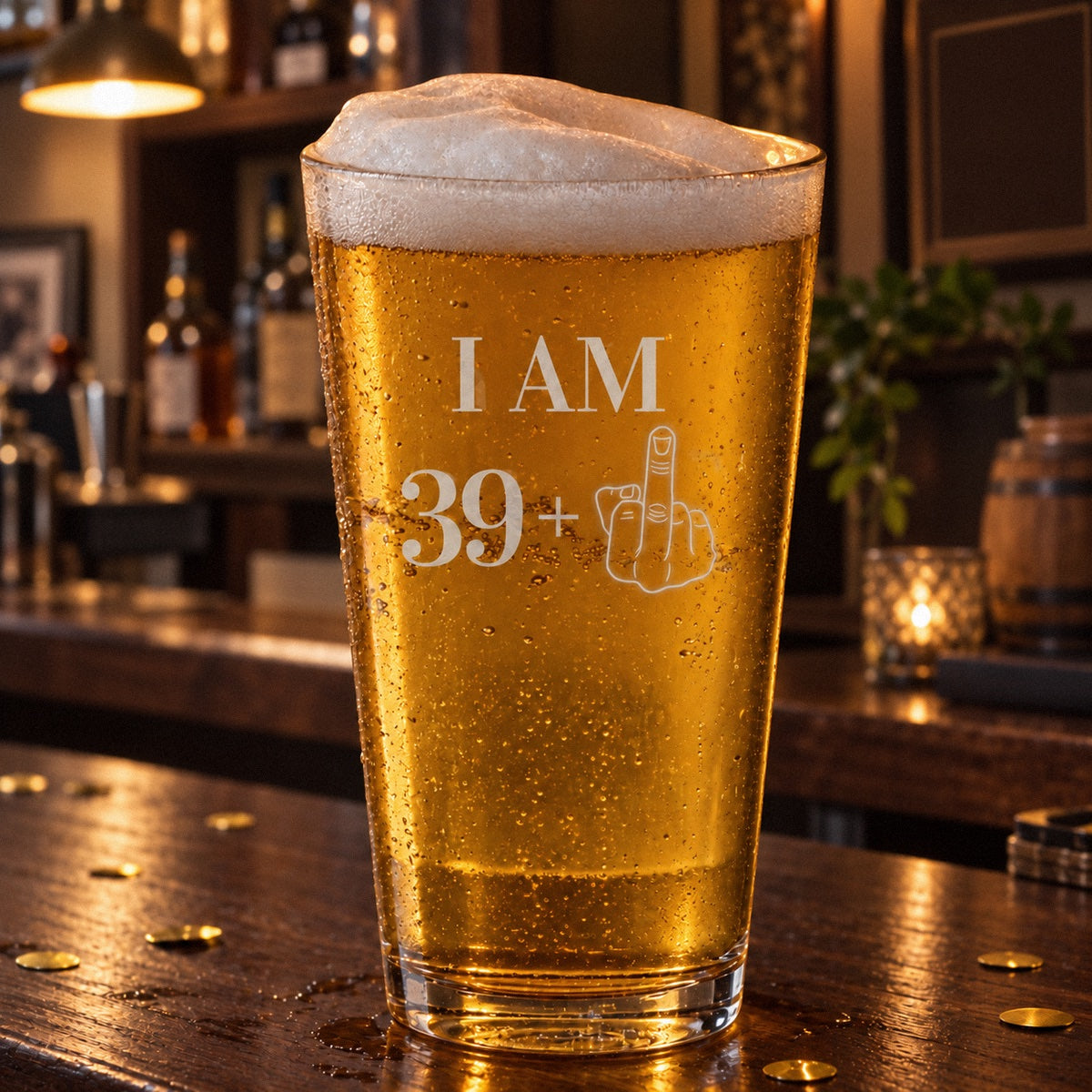 Funny 40th birthday pint glass etched I AM 39 plus a middle finger, a 16 oz pint of lager on a home bar with gold confetti