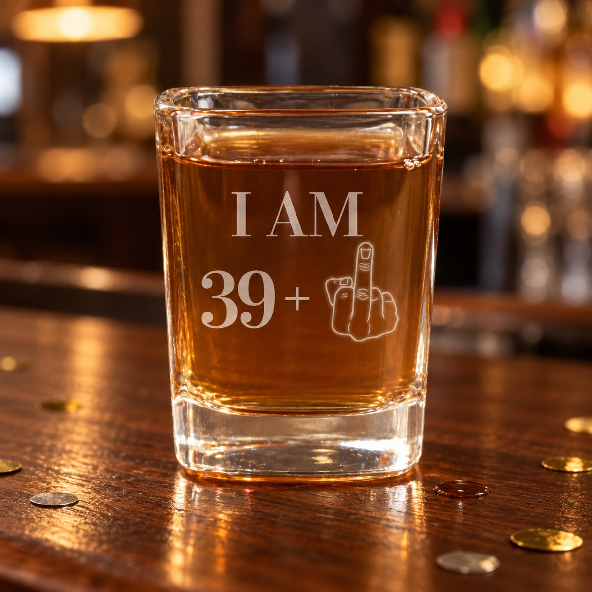 Funny 40th birthday shot glass engraved I AM 39 plus a middle finger, filled with whiskey on a dark walnut bar with gold and silver confetti