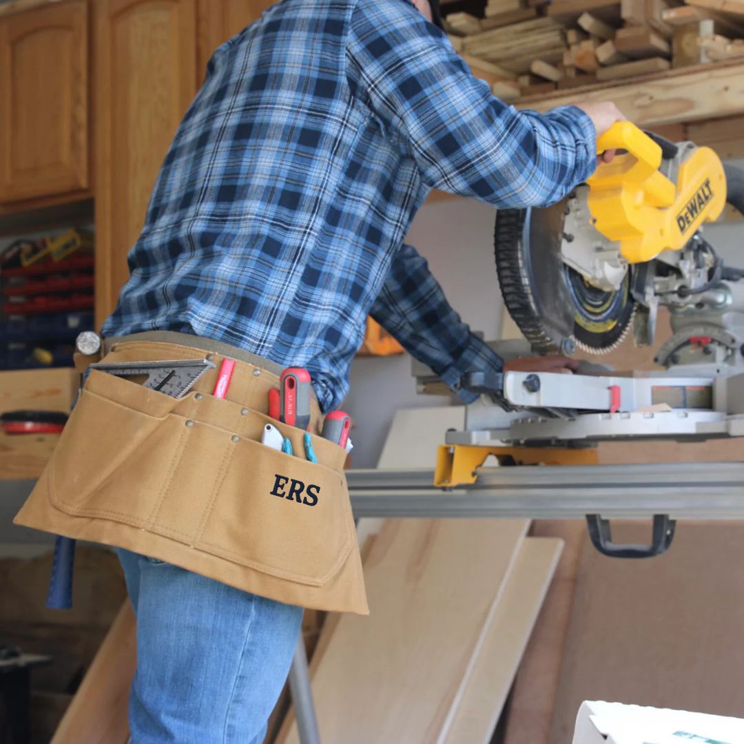 Tan canvas tool belt with sample monogram "ERS" worn during woodworking, filled with various hand tools and accessories in workshop setting