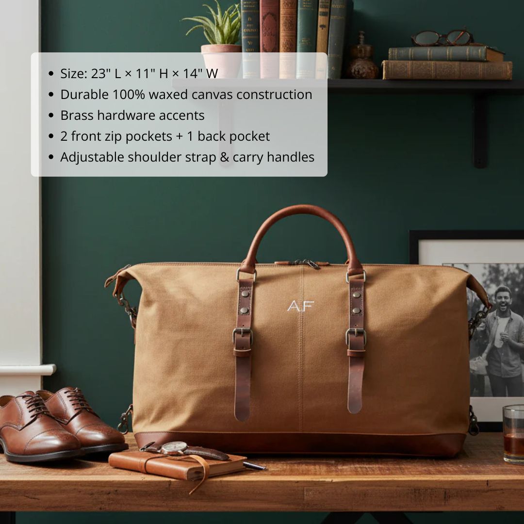 Tan waxed canvas travel bag with brown leather handles and straps, monogrammed with sample initials "AF" on front, displayed on wooden desk with styling accessories