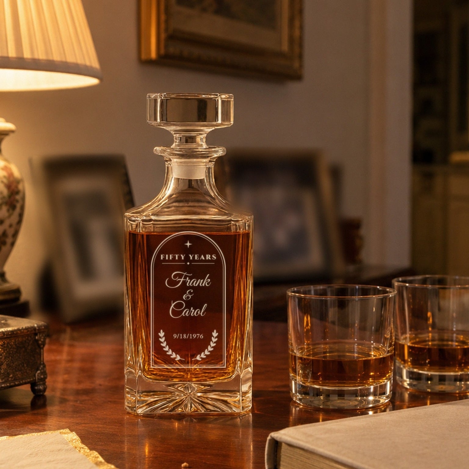 Engraved 50th anniversary decanter for Frank and Carol on a living room sideboard after the party, two bourbons poured beside an old wedding album