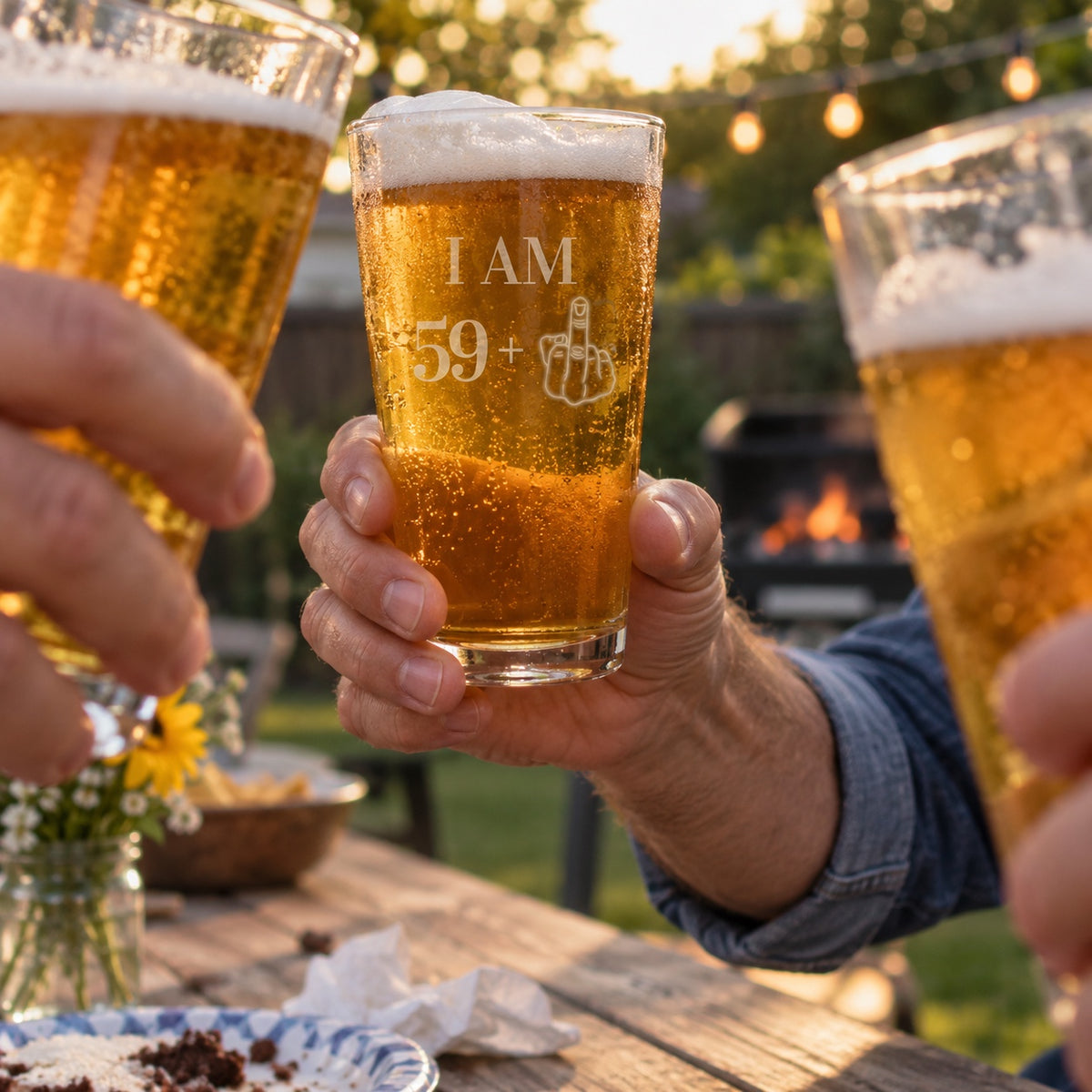 A man raises his I AM 59+ pint glass in a toast at a backyard 60th birthday party, a funny 60th birthday gift for him with friends