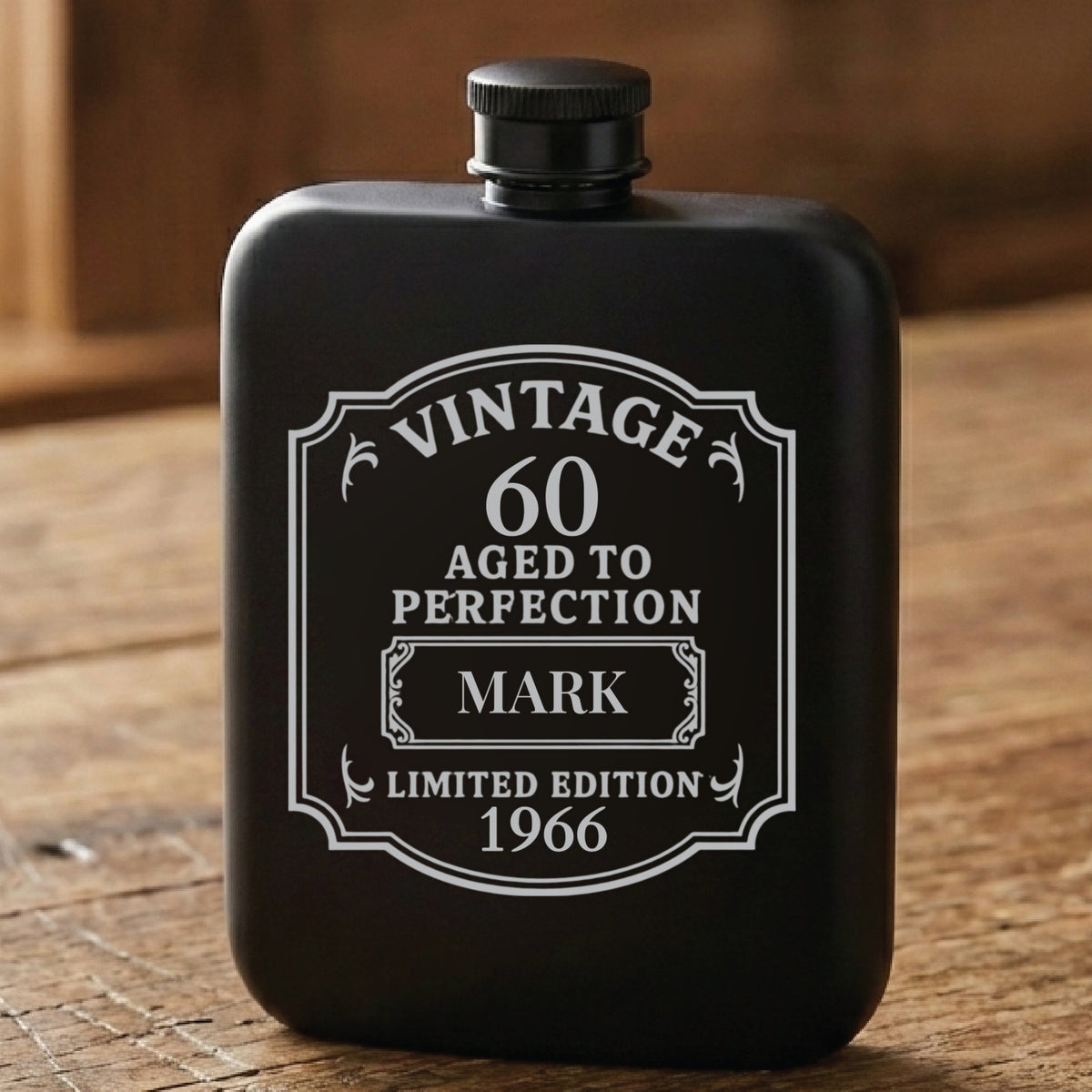 Matte black personalized 60th birthday flask laser engraved with a vintage Aged to Perfection label reading 60, the name Mark and the birth year 1966.