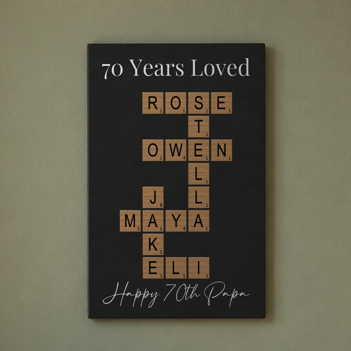 70th birthday gift for men: a 70 Years Loved crossword sign with the grandkids' names and Happy 70th Papa, hanging on a sage green living room wall