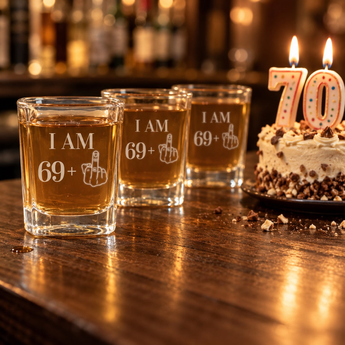 Three 70th birthday shot glasses engraved I AM 69 plus lined up on a bar beside a birthday cake with lit 70 candles