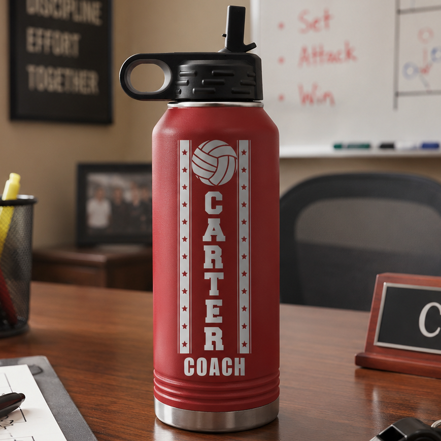 Red insulated water bottle with black flip-top lid, engraved with volleyball icon and "CARTER COACH" text with star design, displayed on wooden desk in office setting.