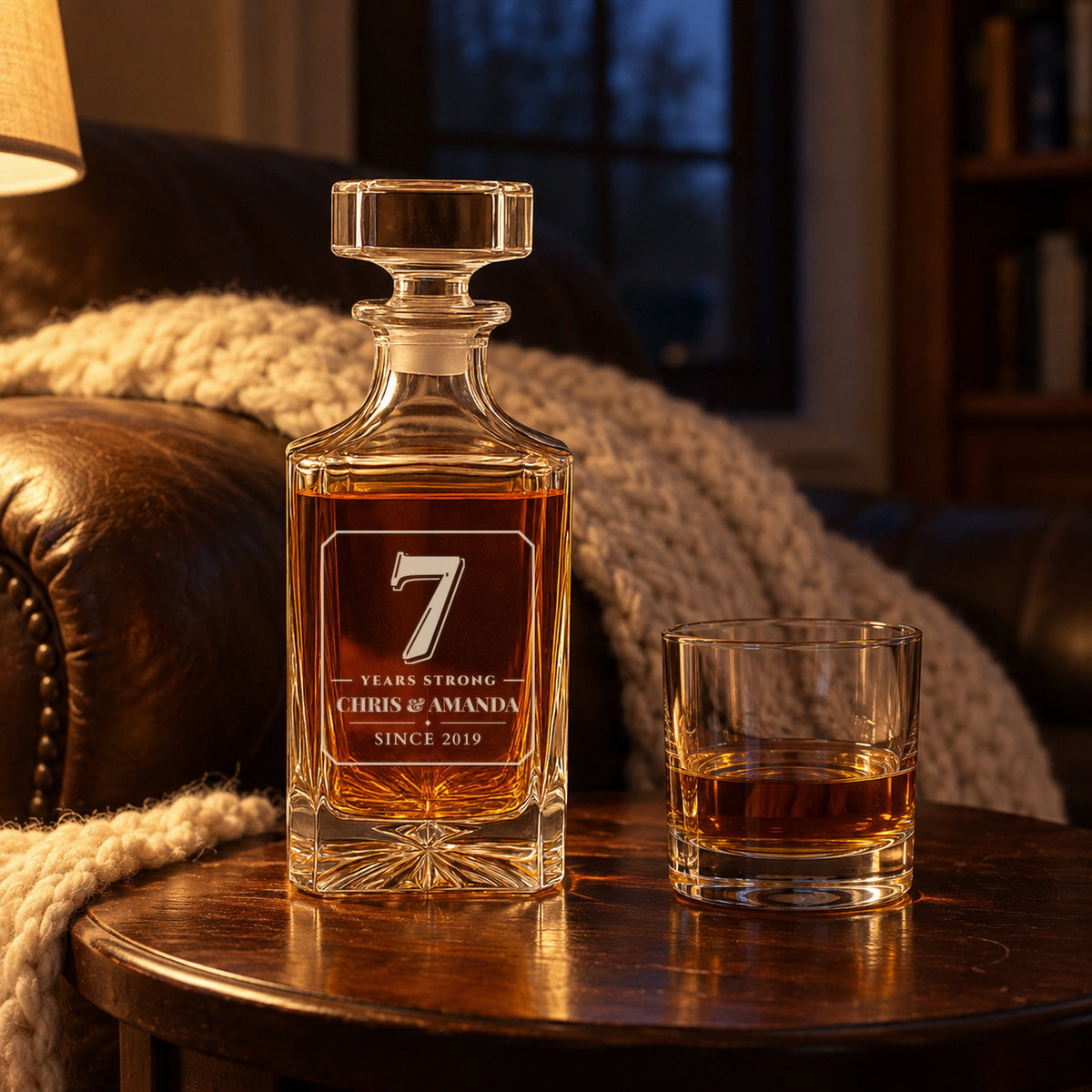Personalized decanter engraved 7 Years Strong, Chris & Amanda, on a side table by a cream wool throw, a 7th anniversary gift for husband