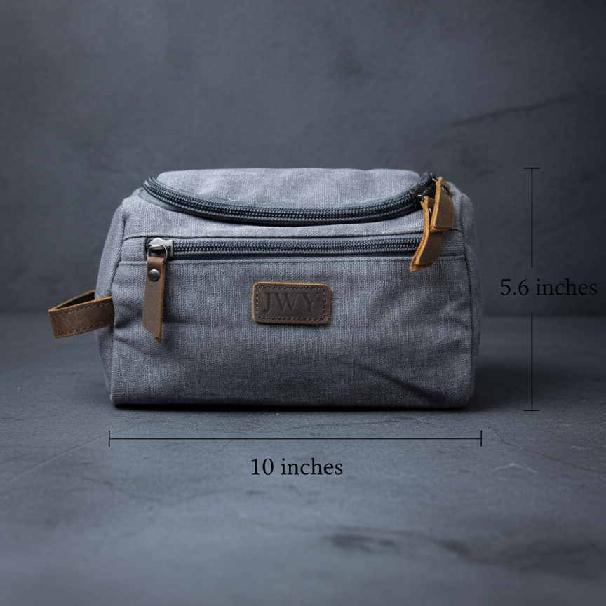 Gray canvas toiletry bag with brown leather trim and accents, featuring sample "JWY" engraved leather patch, dual zippered compartments, and side handles, measured at 10 by 5.6 inches