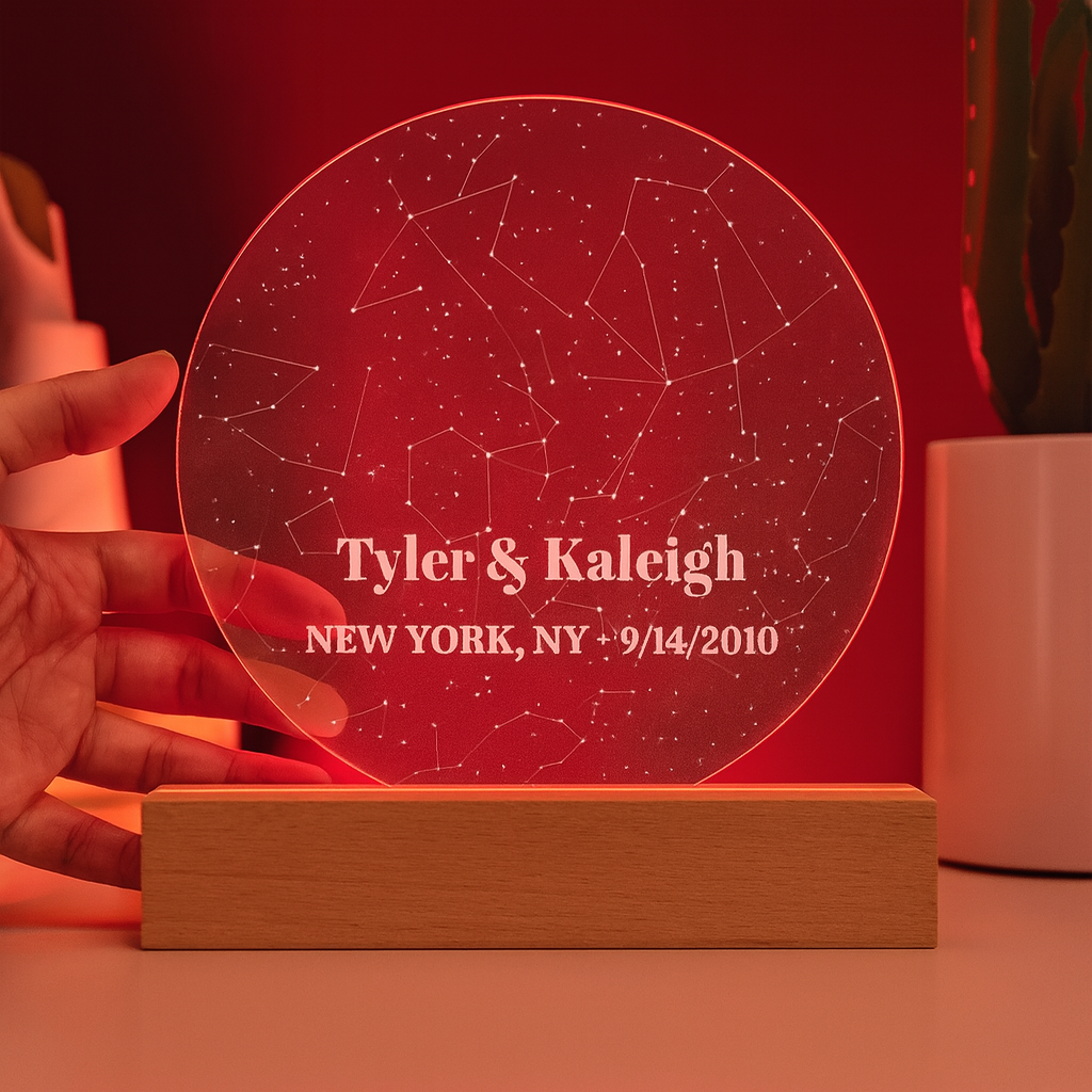 Star map plaque with laser-engraved constellation pattern and sample personalization reading "Tyler & Kaleigh, NEW YORK, NY • 9/14/2010" mounted on wooden base with red LED lighting