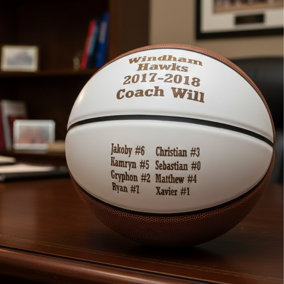 Basketball engraved with sample text "Windham Hawks 2017-2018 Coach Will" and player roster with names and numbers on white panel.